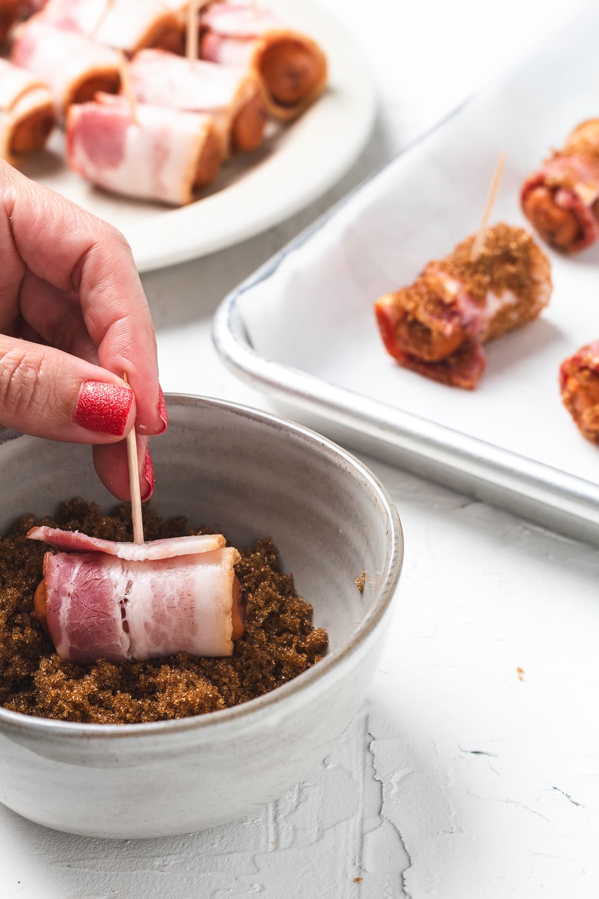 Hand rolling bacon-wrapped sausage in brown sugar.