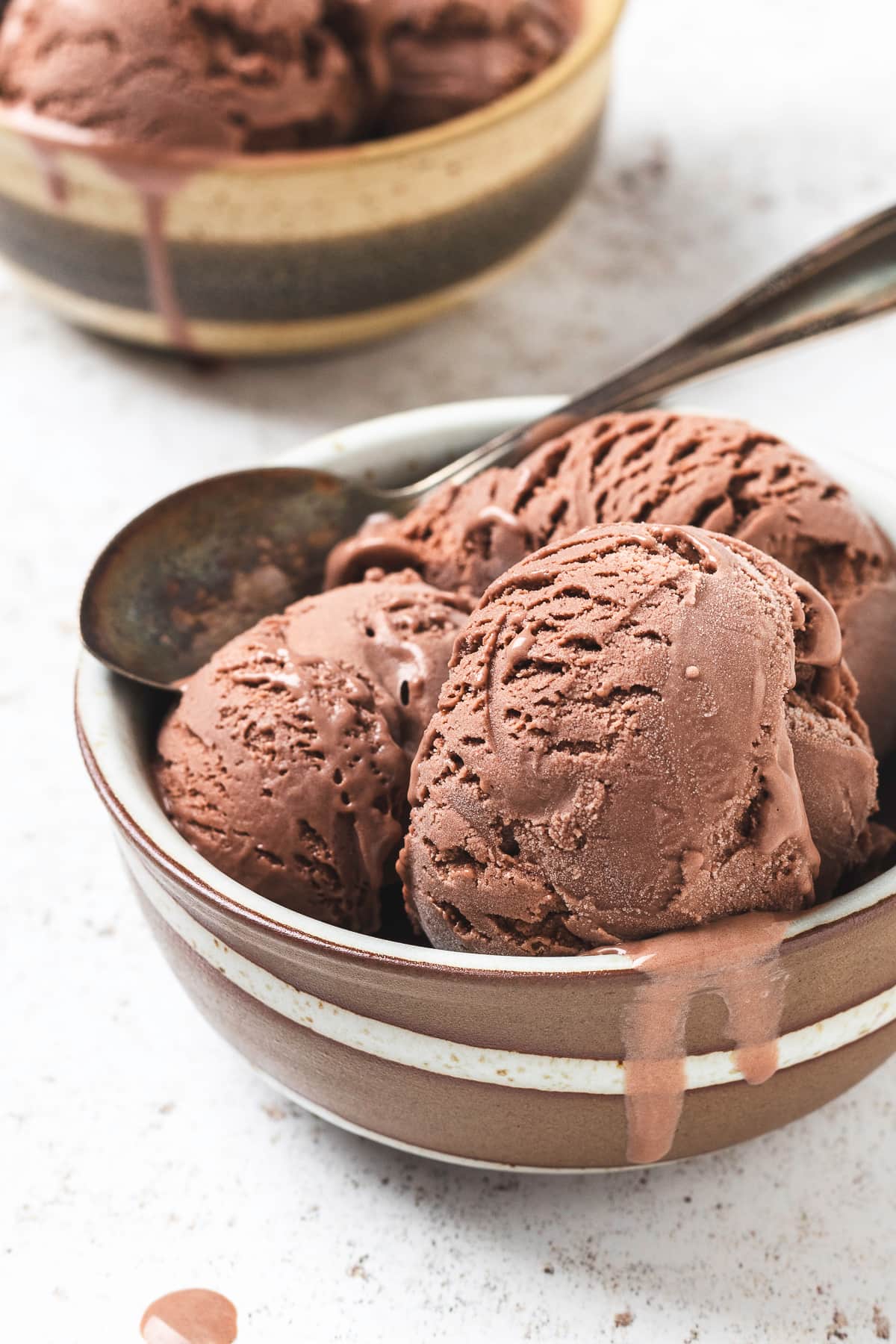 Two bowls of chocolate ice cream on a light colored background.