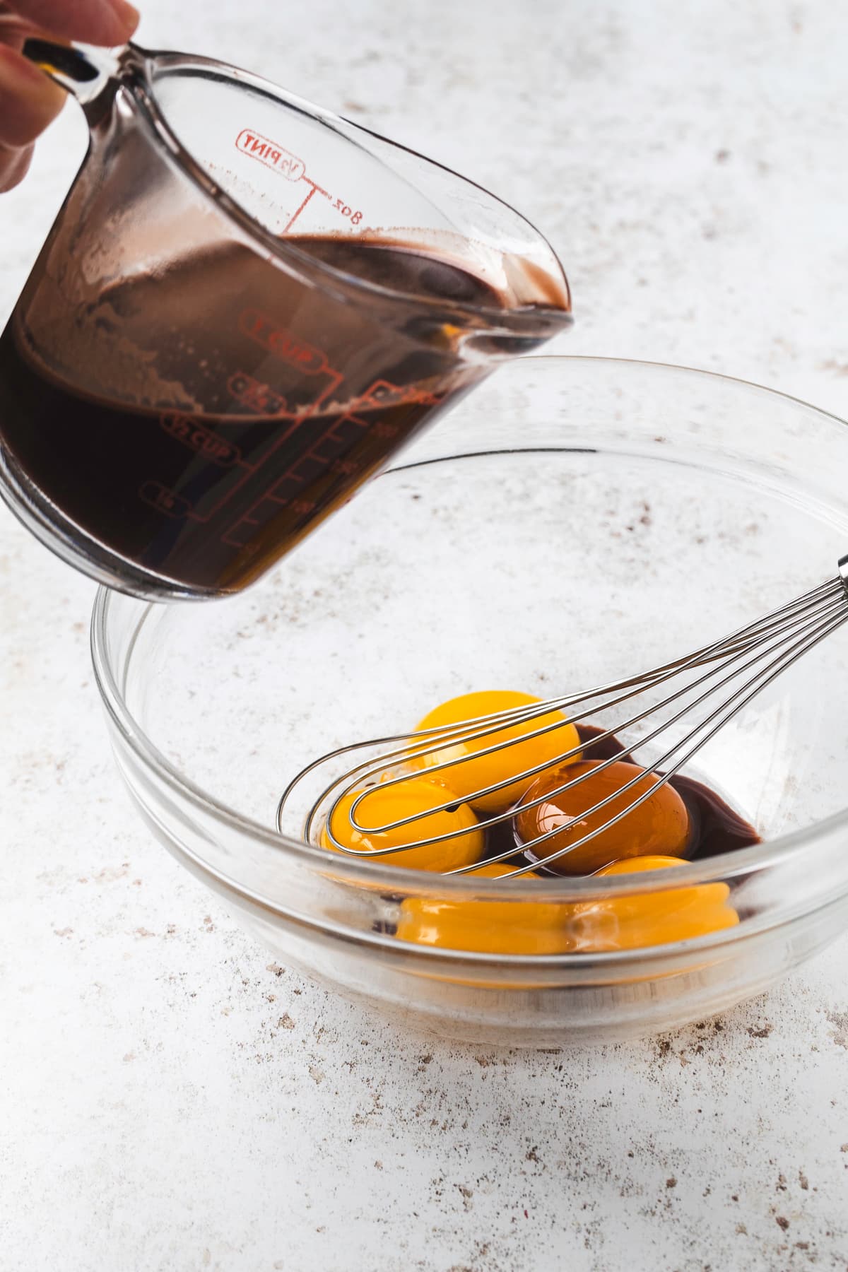 Adding chocolate, milk, and sugar mixture to a bowl full of yolks.