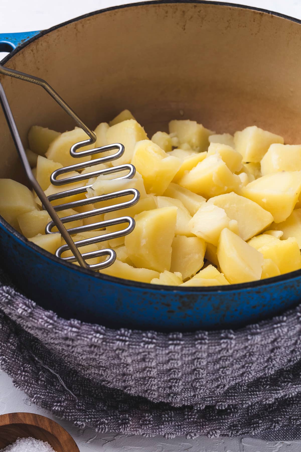 Mashing potatoes in a blue Dutch oven.