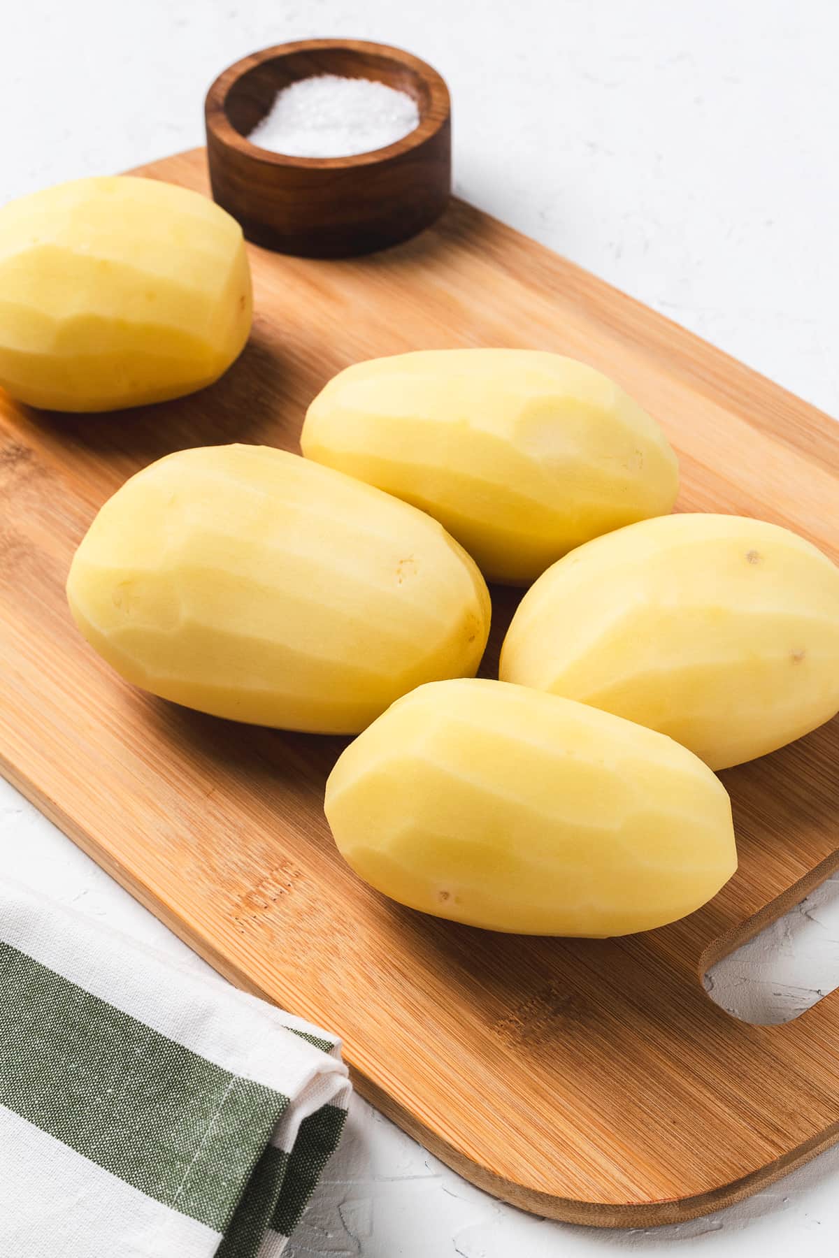 Peeled yellow potatoes on a cutting board.