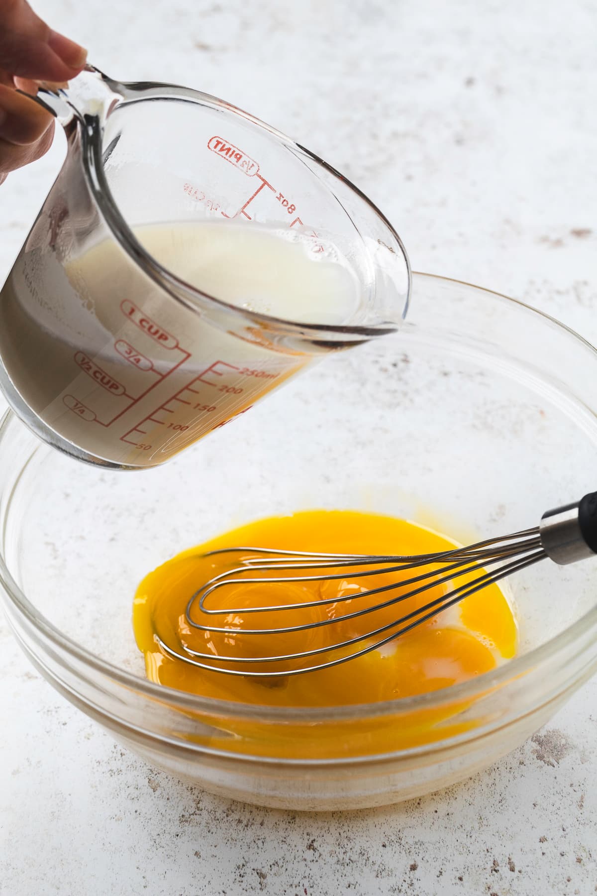 Adding warm sugar-infused milk to a bowl filled with egg yolks.