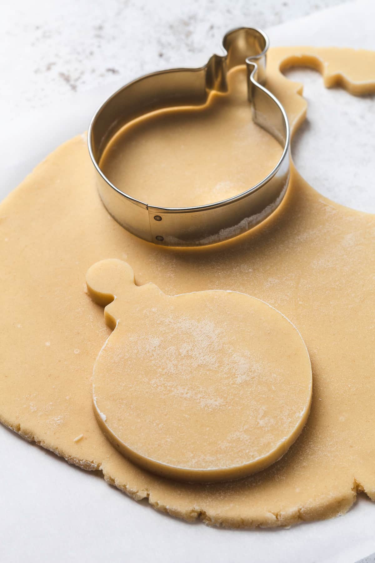 Round ornament-shaped sugar cookie cut out from dough on a floured surface.