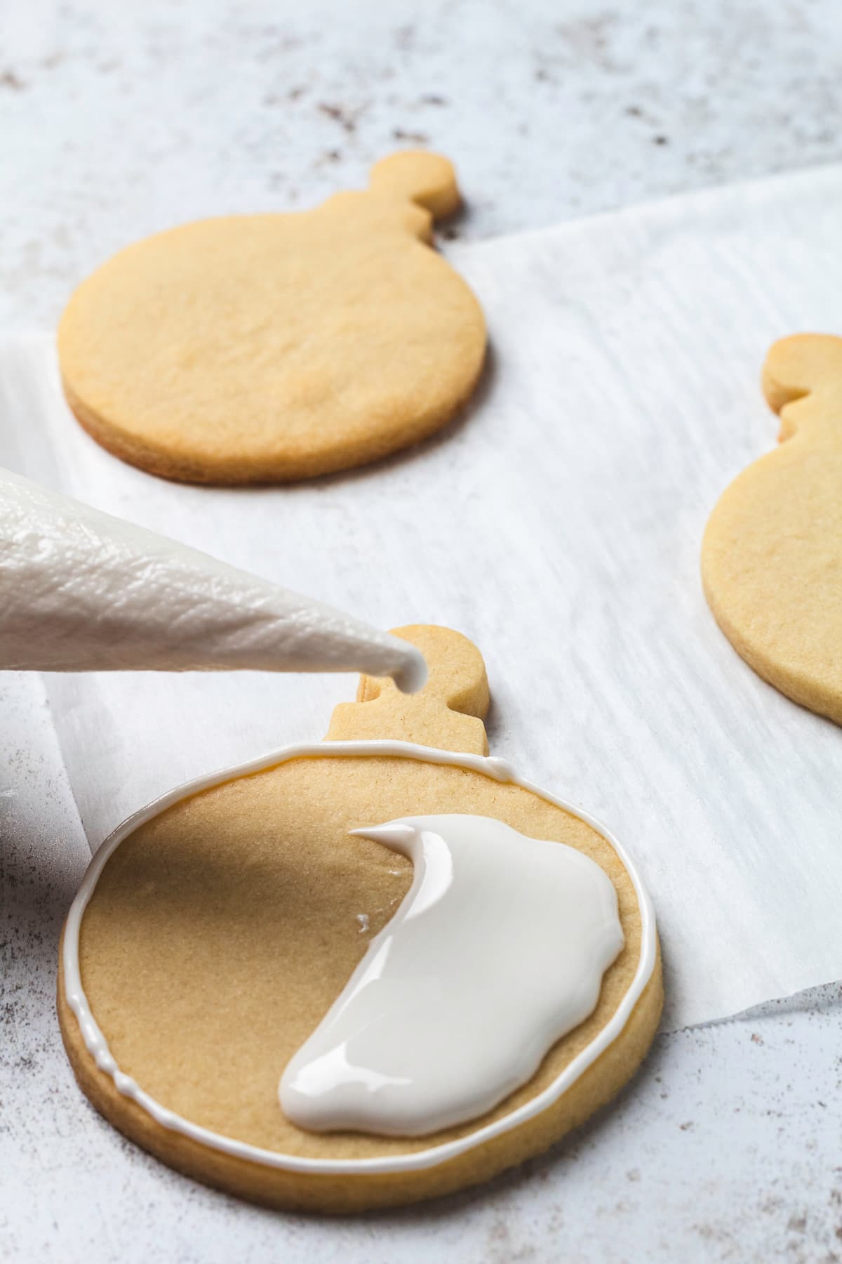 White icing flooding the center of a round ornament sugar cookie.