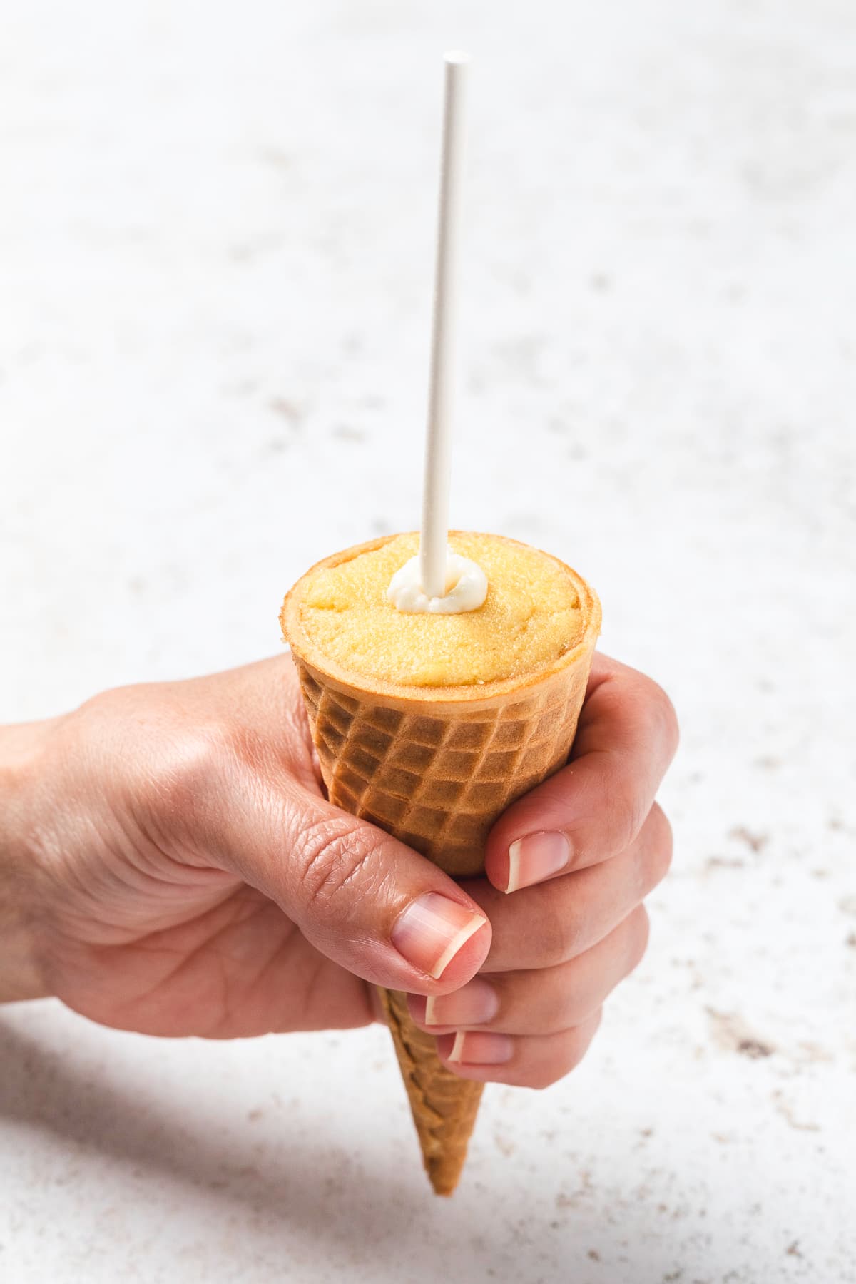 Hand holding a sugar cone filled with cake pop mixture and stick added.