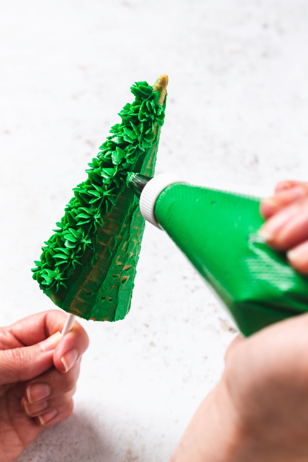 Hand holding piping bag adding texture to Christmas tree cake pop.