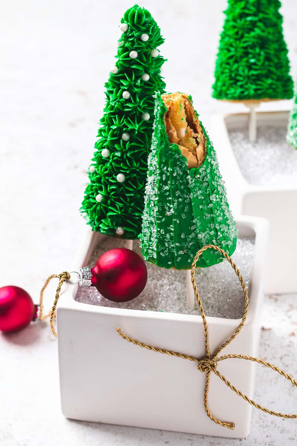 Christmas tree cake pops in a white box, one with a bite taken out.