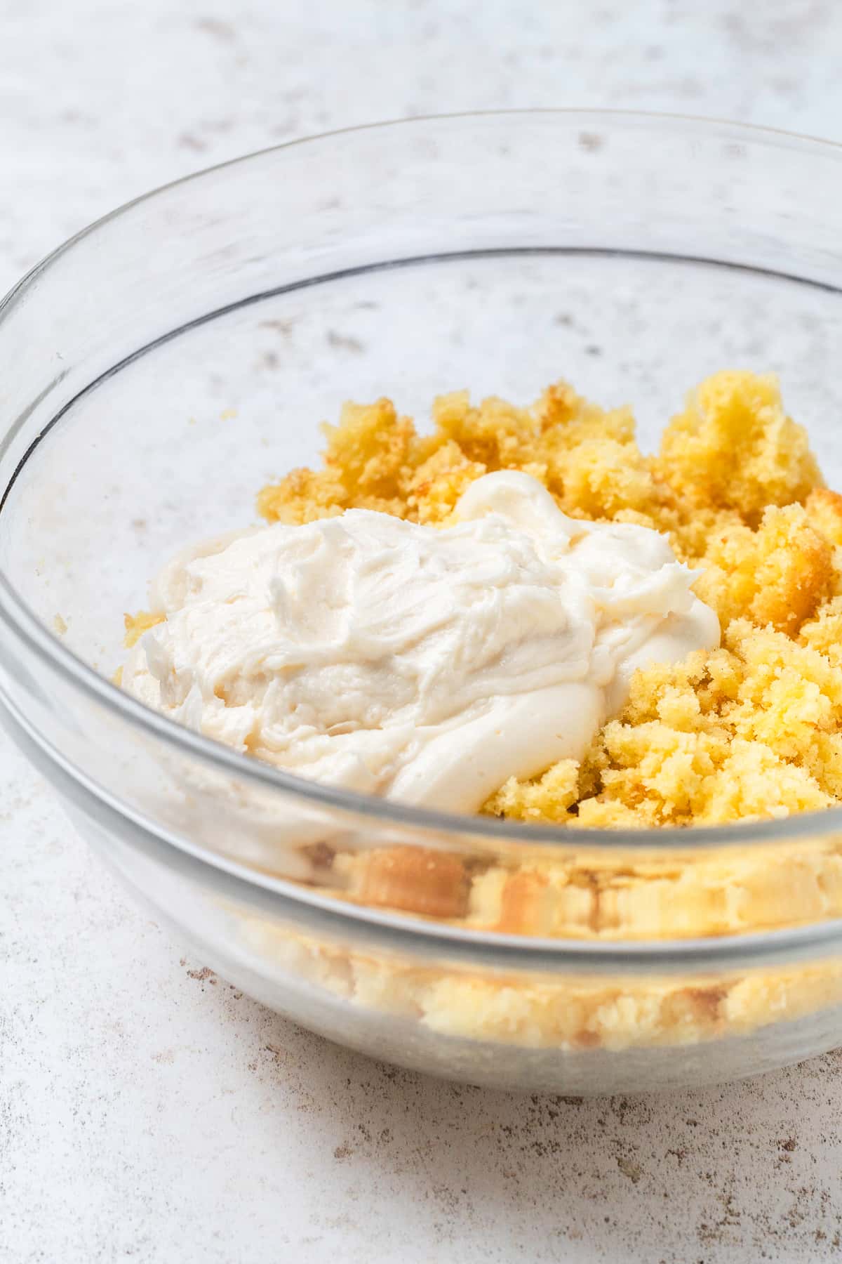 Vanilla buttercream frosting and crumbled yellow cake in a clear mixing bowl.