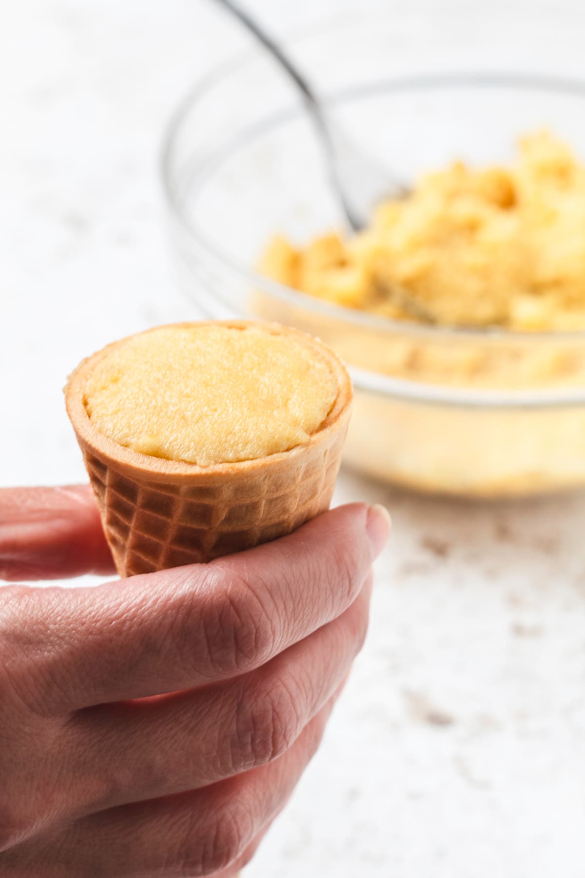 Hand holding cake pop mixture stuffed inside a sugar cone.