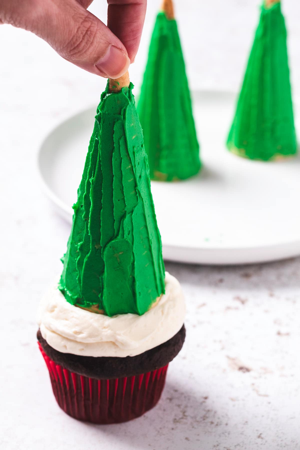 Hand placing green frosted sugar cones on top of cupcake.
