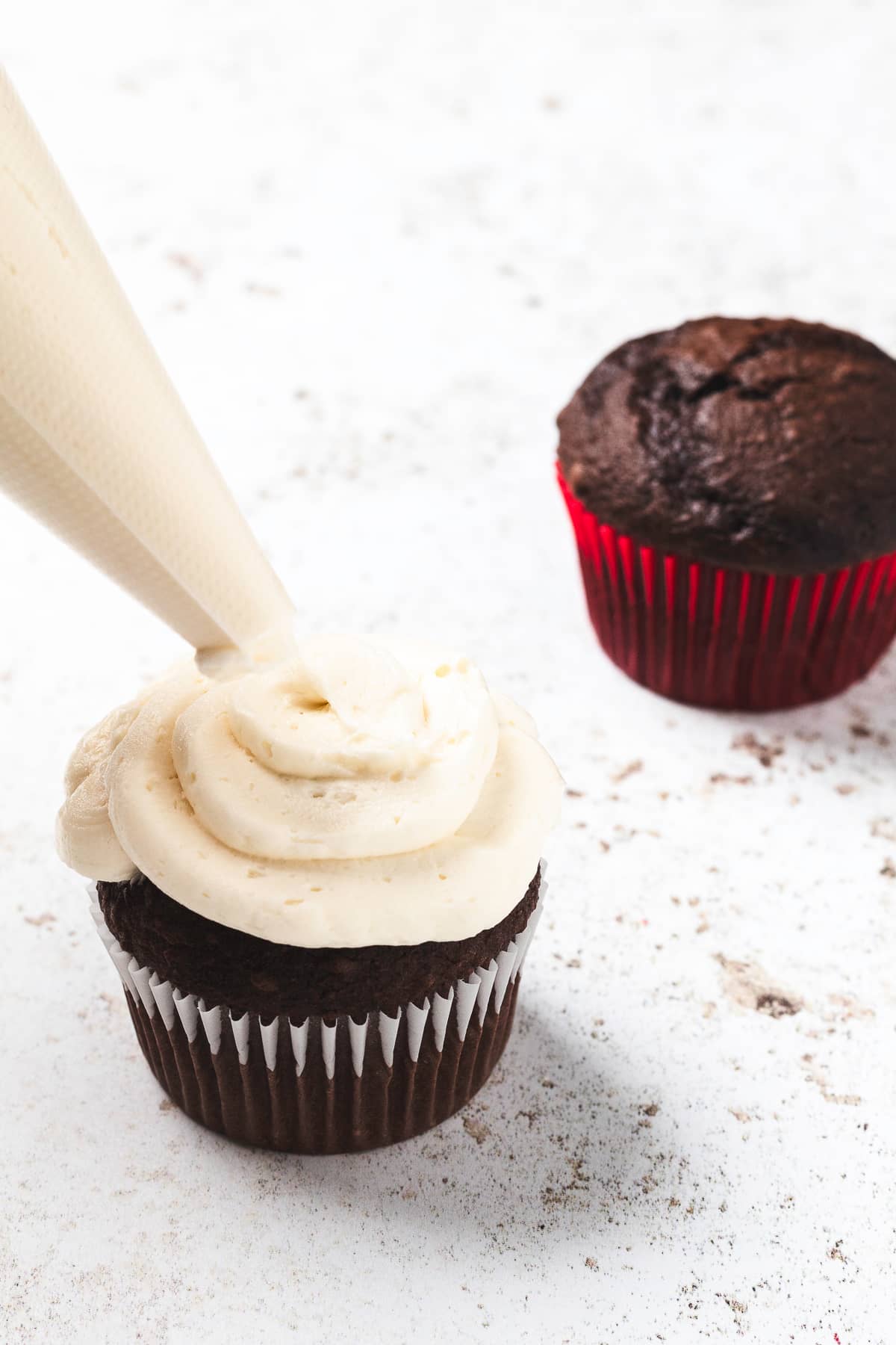Adding vanilla frosting on top of chocolate cupcake.