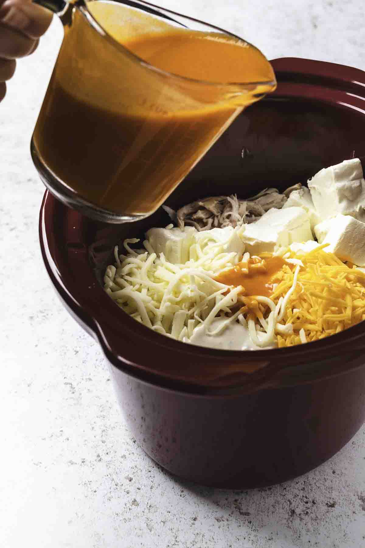 Ingredients for buffalo chicken dip added to slow cooker.