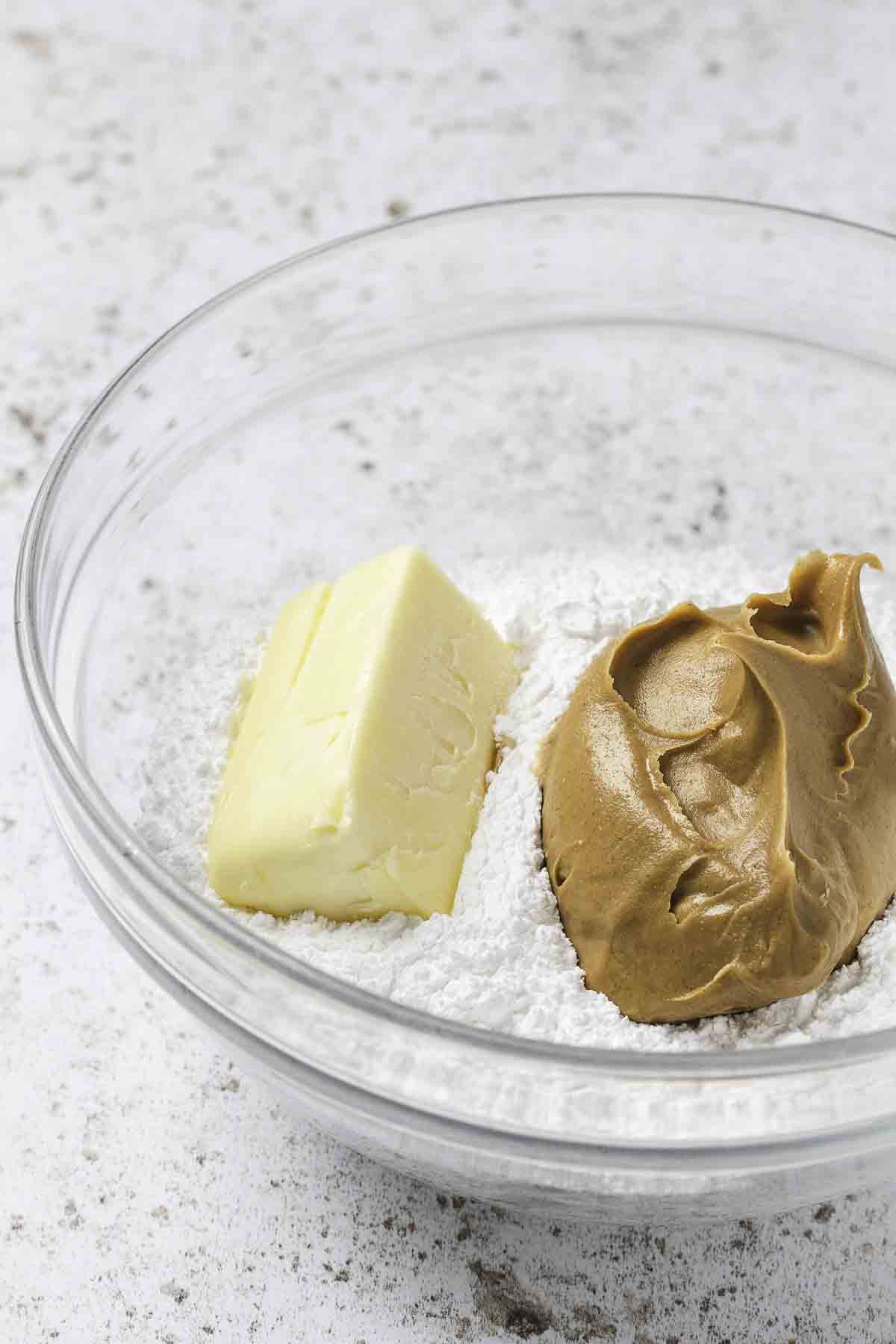 Peanut butter, butter, and powdered sugar in a clear bowl.