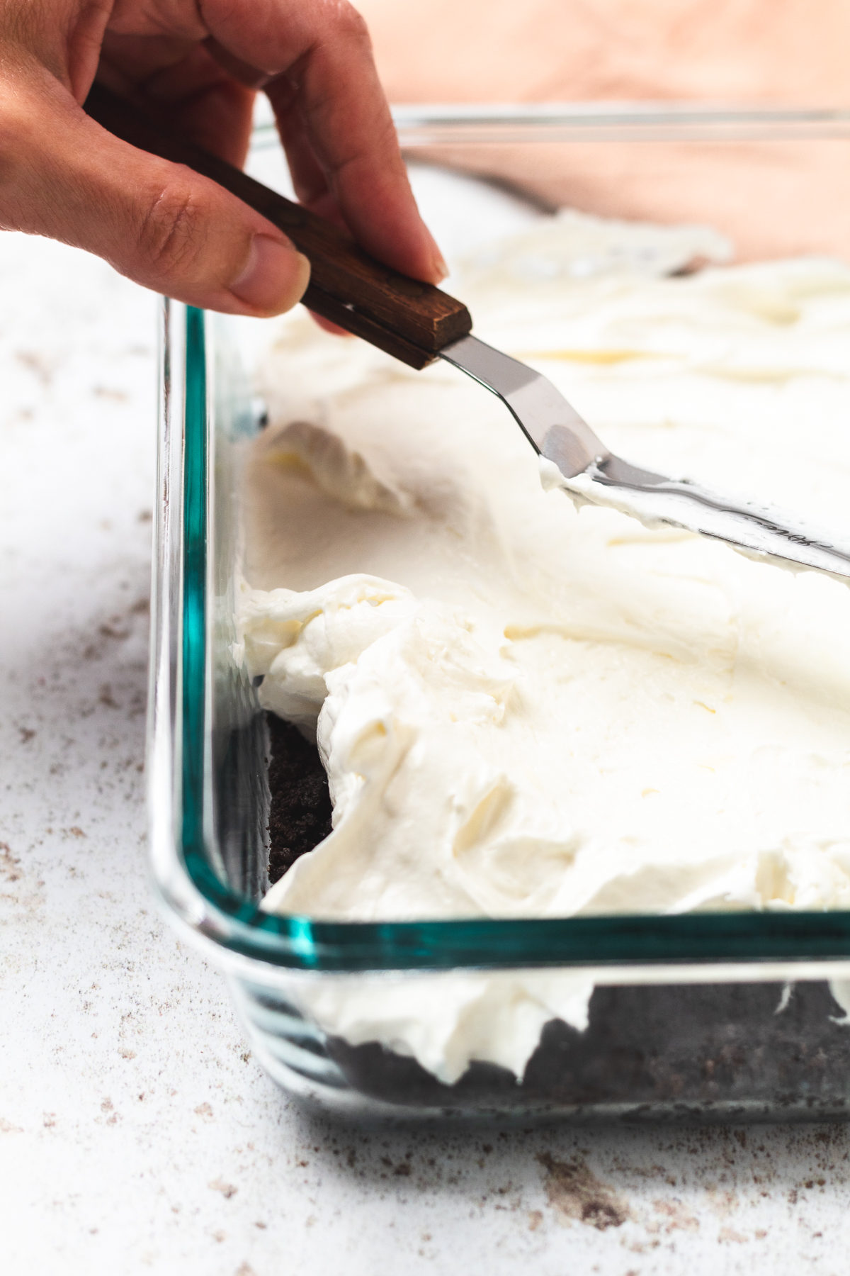 Adding a smooth cream cheese layer over the Oreo crust in a glass baking dish.