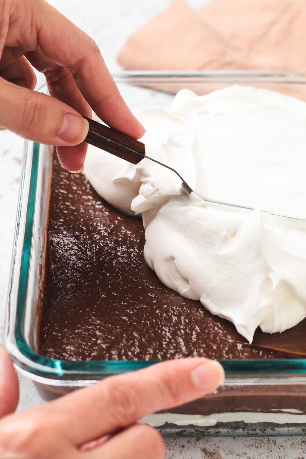 Spreading fluffy whipped topping over a set chocolate pudding layer in Oreo delight dessert.