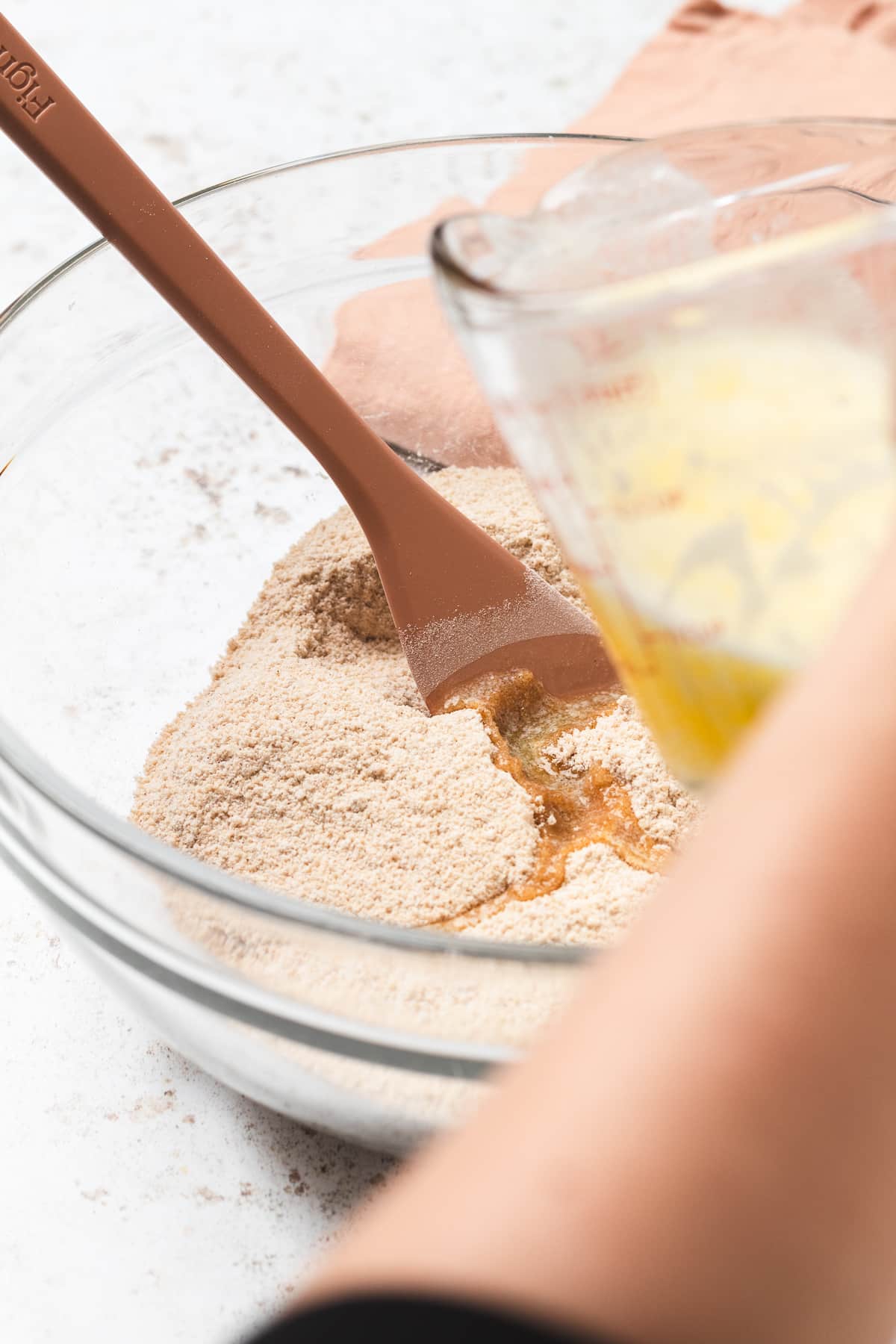 Pouring melted butter into dry crumble ingredients in a glass bowl.