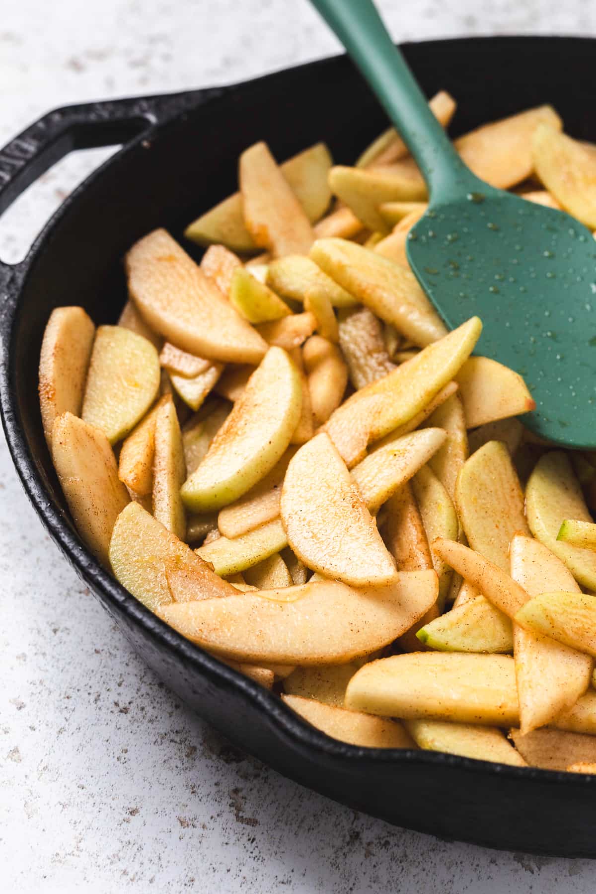 Sliced apples mixed with spices in a cast iron skillet, ready to cook.