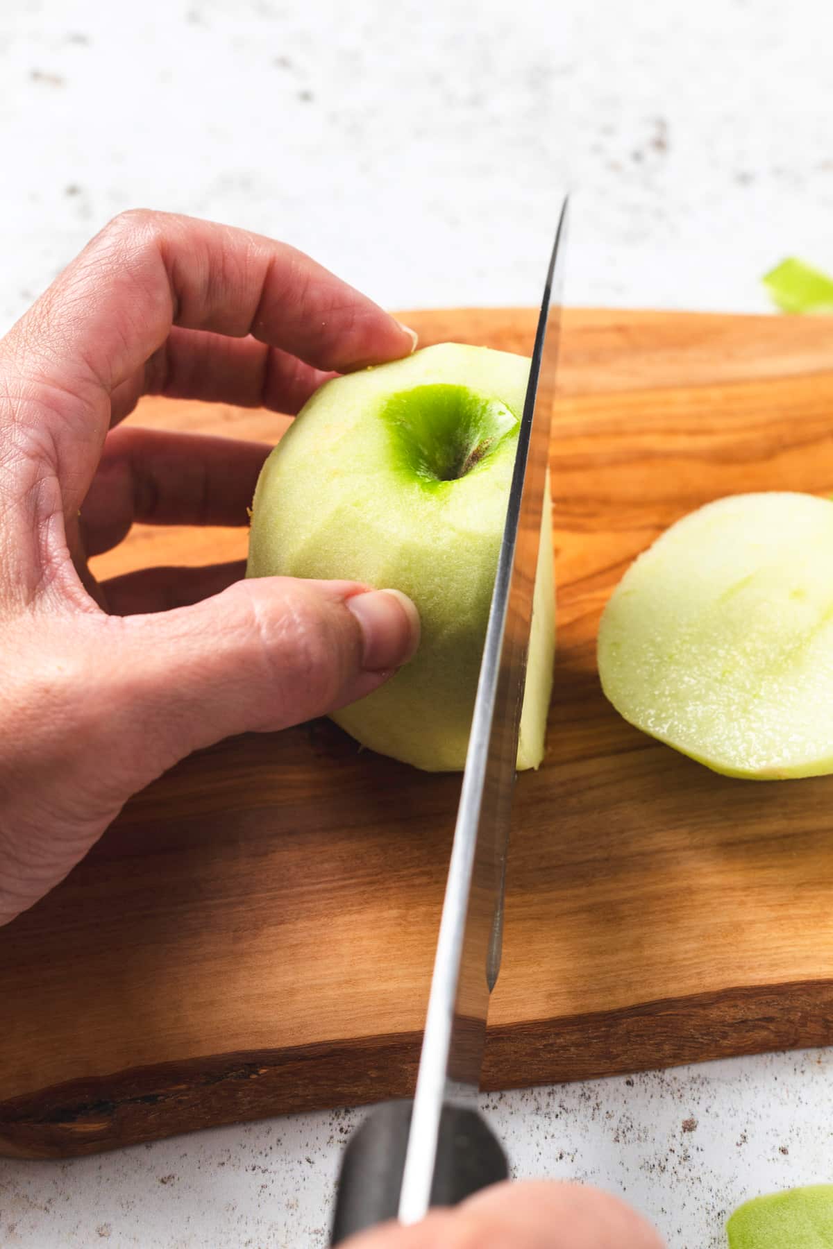 Hand slicing a peeled green apple on a wooden cutting board with a knife.