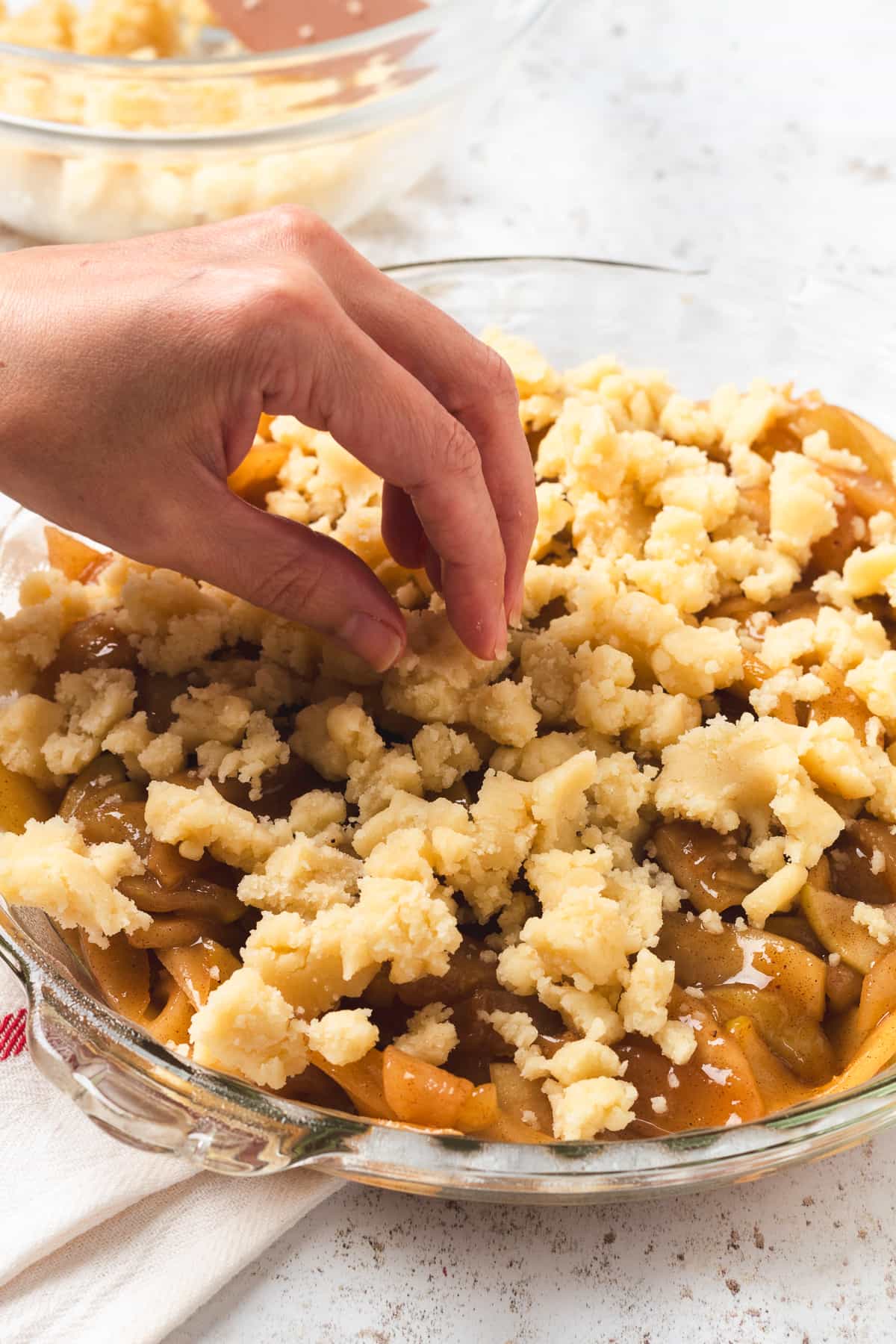 Sprinkling buttery crumble topping over sweet caramel apple filling in a pie dish, ready for baking.