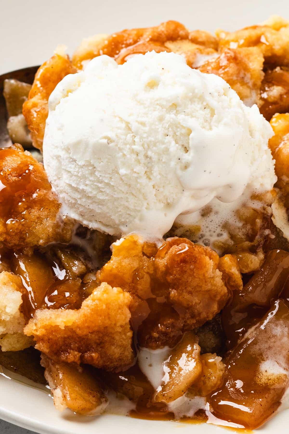 Close-up of caramel apple cobbler with vanilla ice cream melting into the warm, spiced filling.
