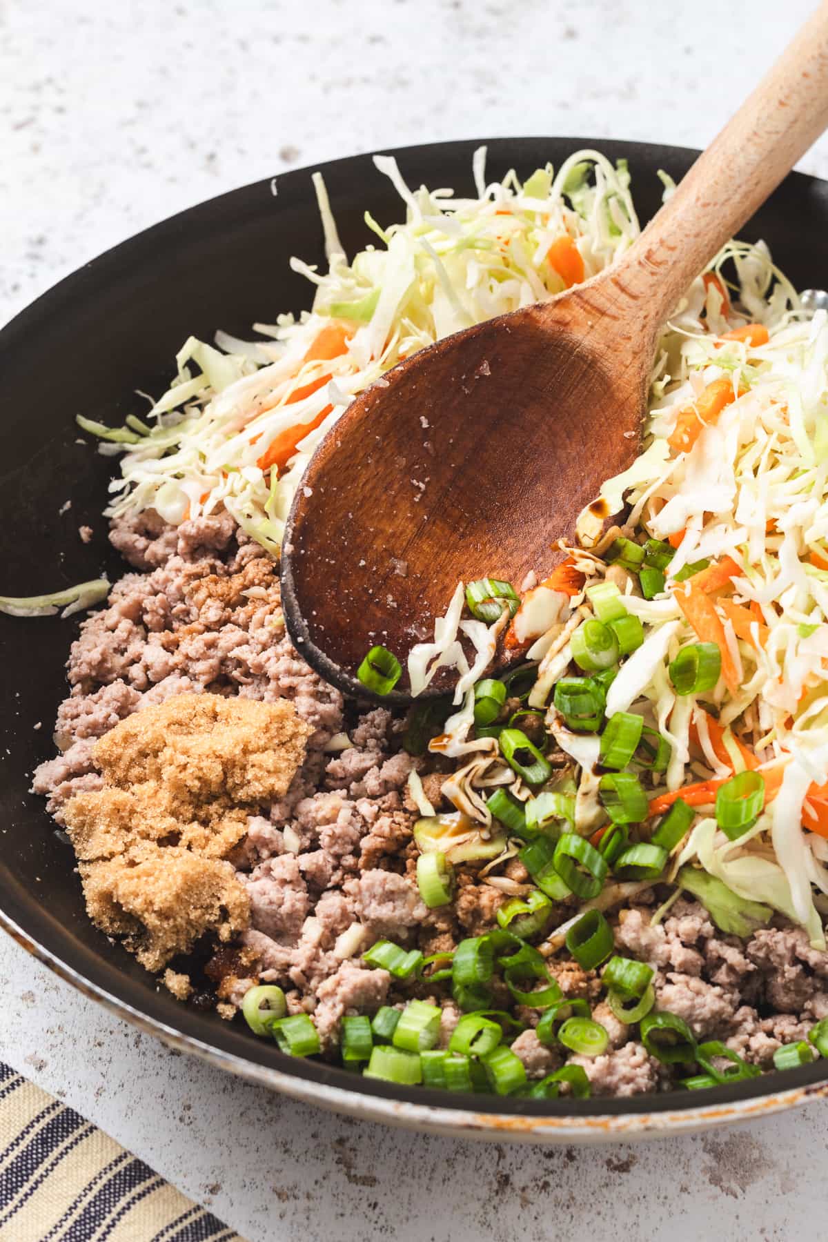 Ground turkey, cabbage, carrots, green onions, and brown sugar in a skillet with a wooden spoon.