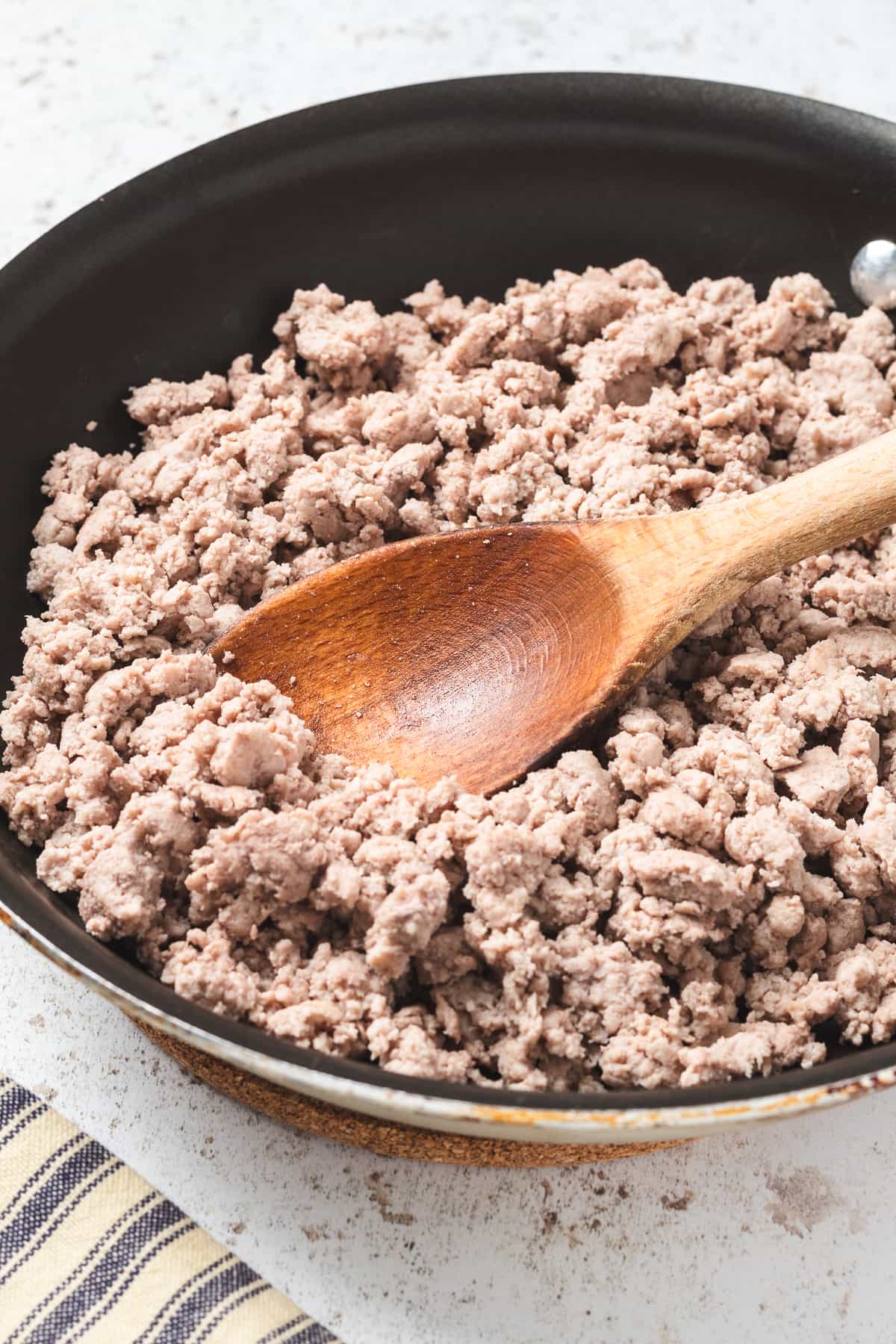 Cooked ground turkey in a skillet with a wooden spoon.
