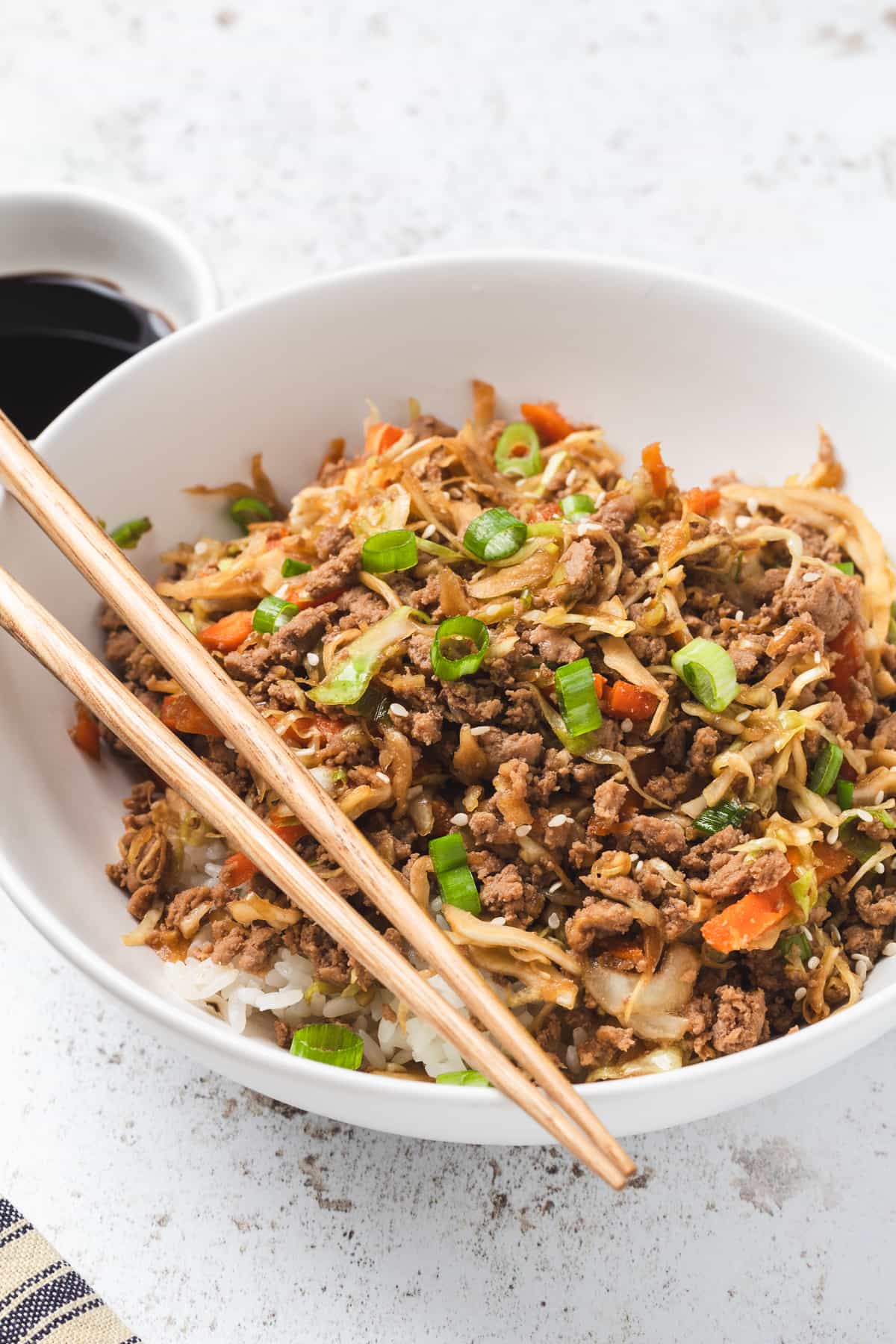 Egg roll in a bowl served over rice in a white bowl with chopsticks, garnished with green onions.