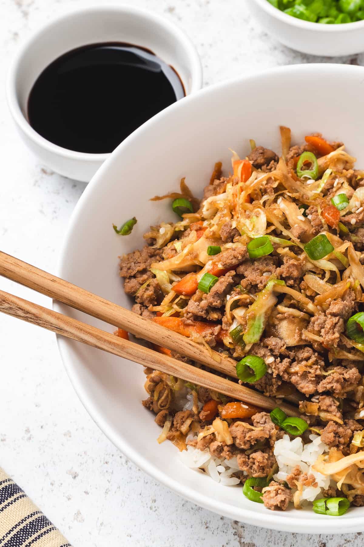Egg roll in a bowl served over rice in a white bowl with chopsticks, garnished with green onions.