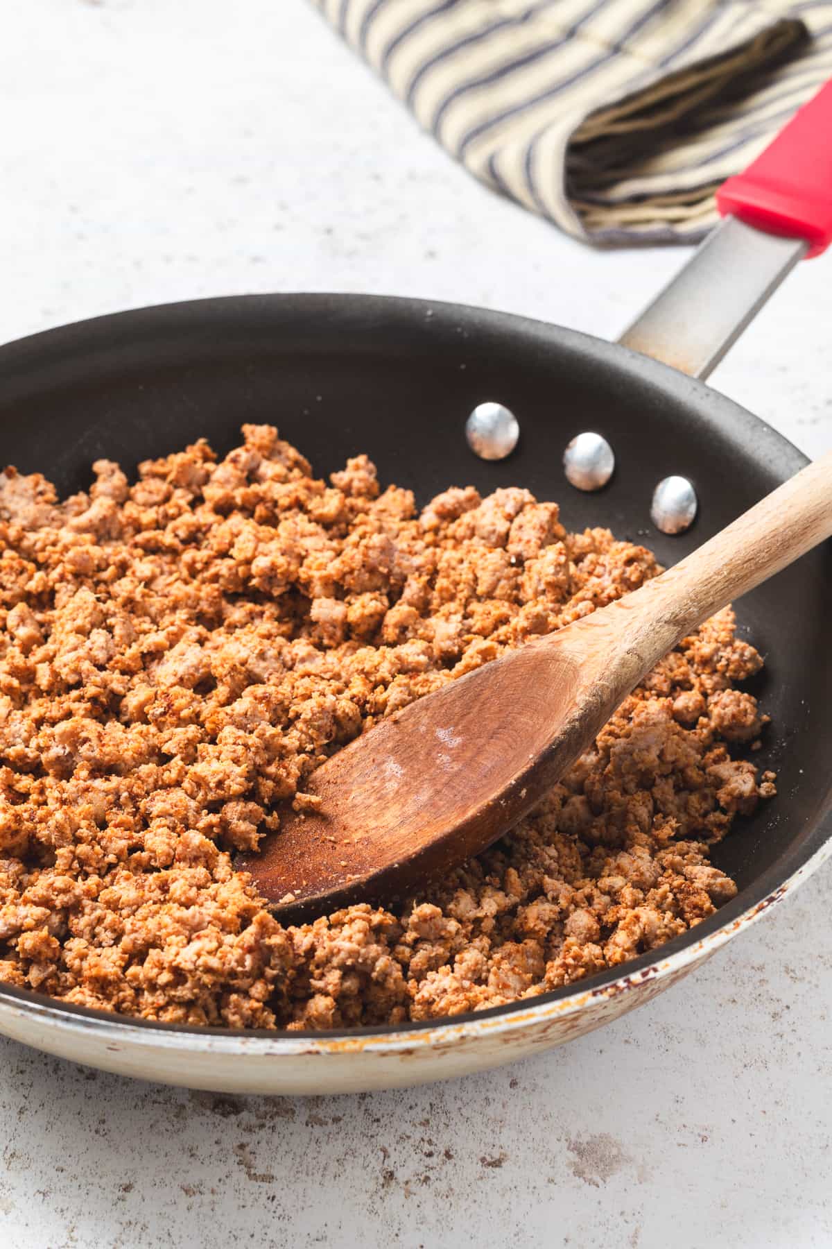 Cooked and seasoned ground turkey in skillet, stirred with wooden spoon.