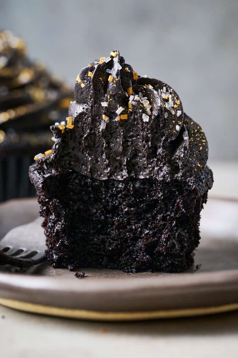 Black velvet cupcake with tall black frosting swirl and gold sprinkles on top.