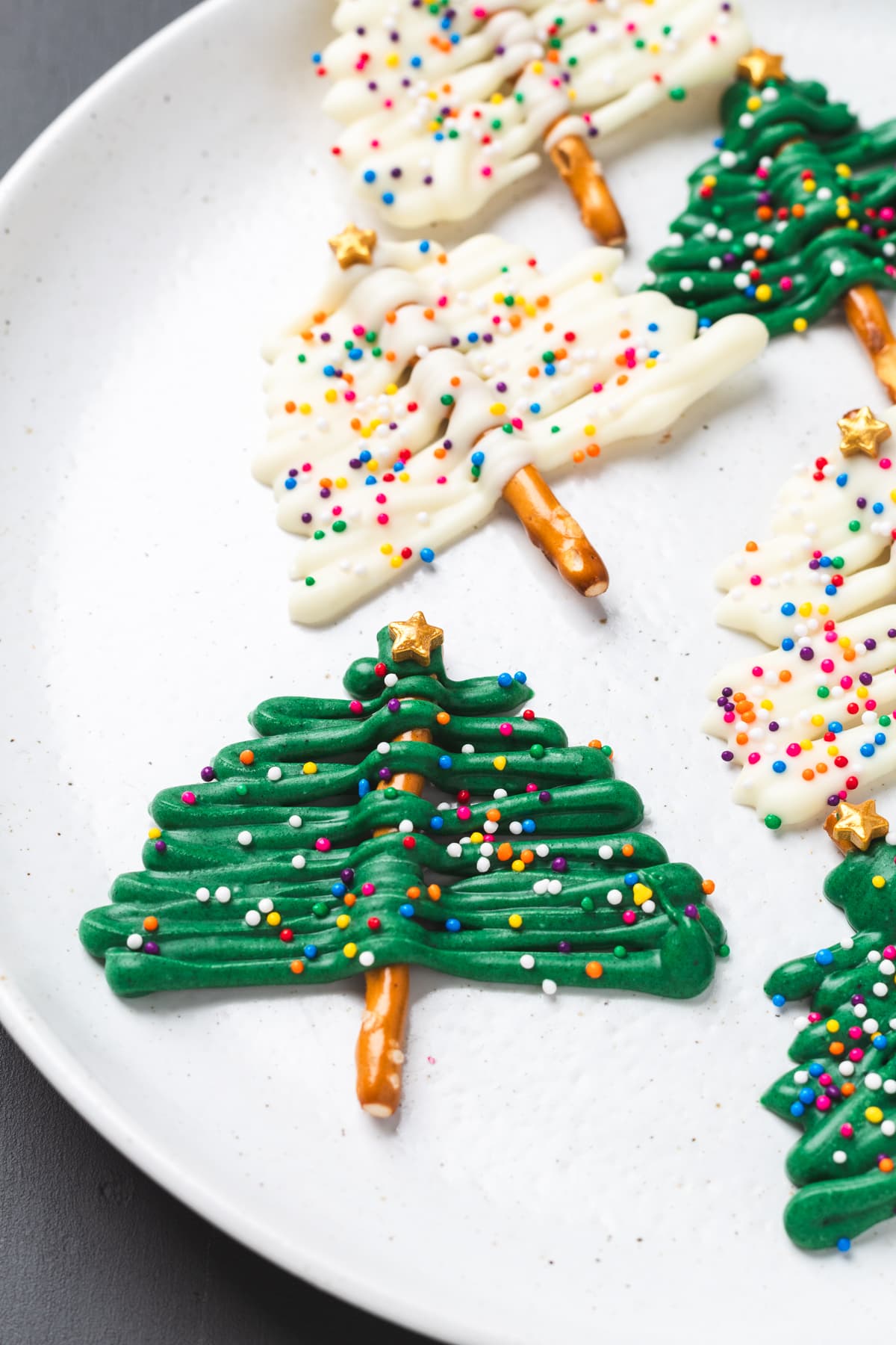 Plate of green and white chocolate Christmas tree pretzels topped with sprinkles and gold stars.