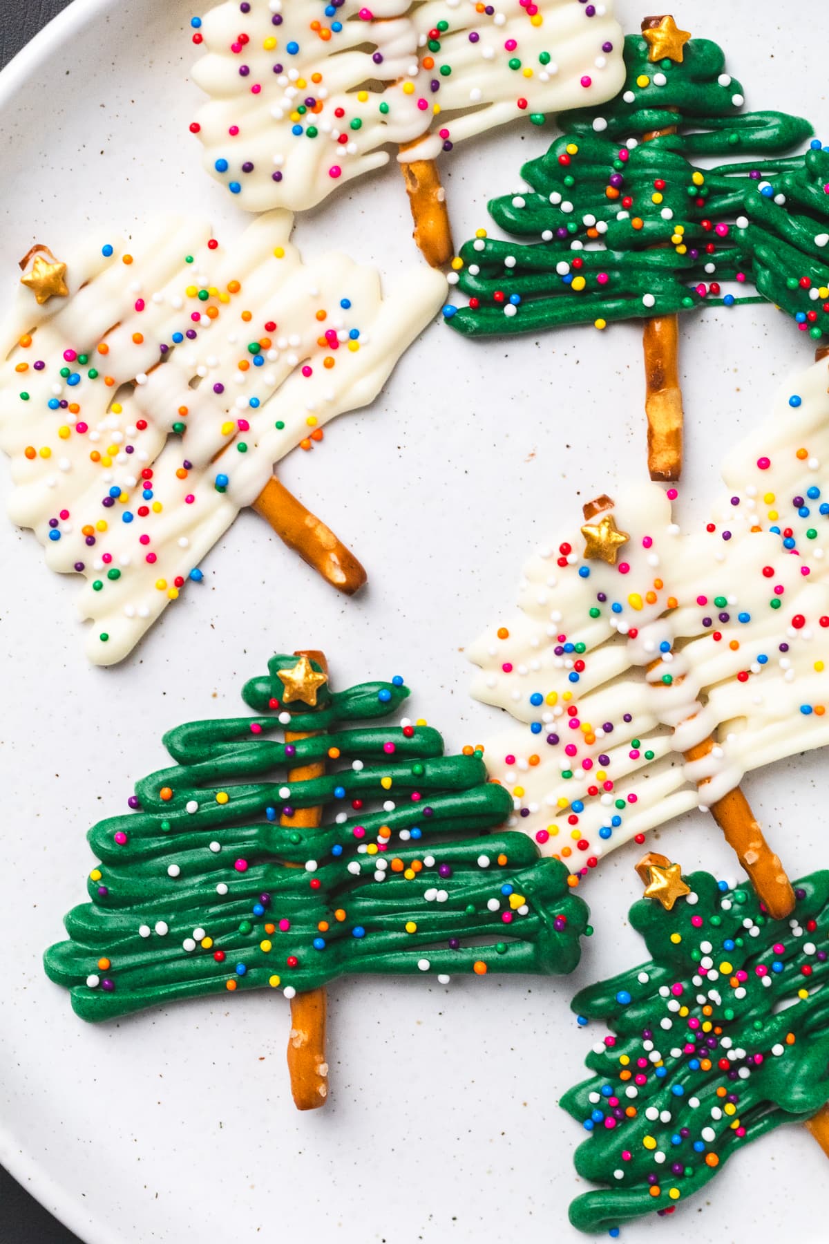 White and green chocolate Christmas tree pretzels with sprinkles and gold stars on a plate.