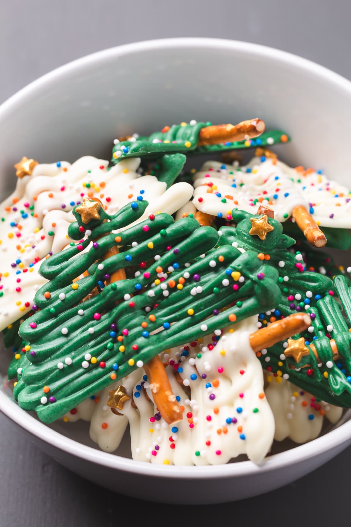 Bowl filled with green and white chocolate Christmas tree pretzels decorated with sprinkles.