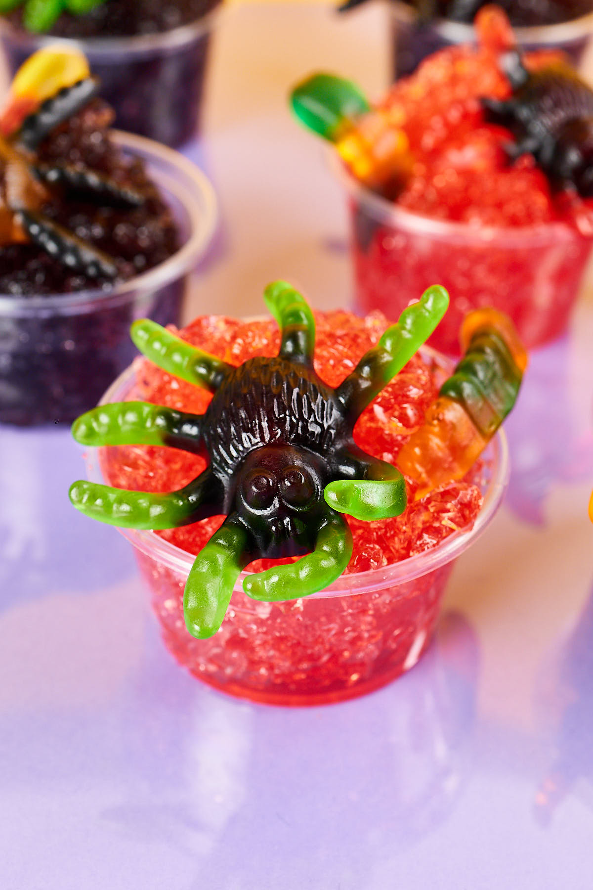 Halloween jello cups topped with gummy worms and plastic spiders for a spooky treat.