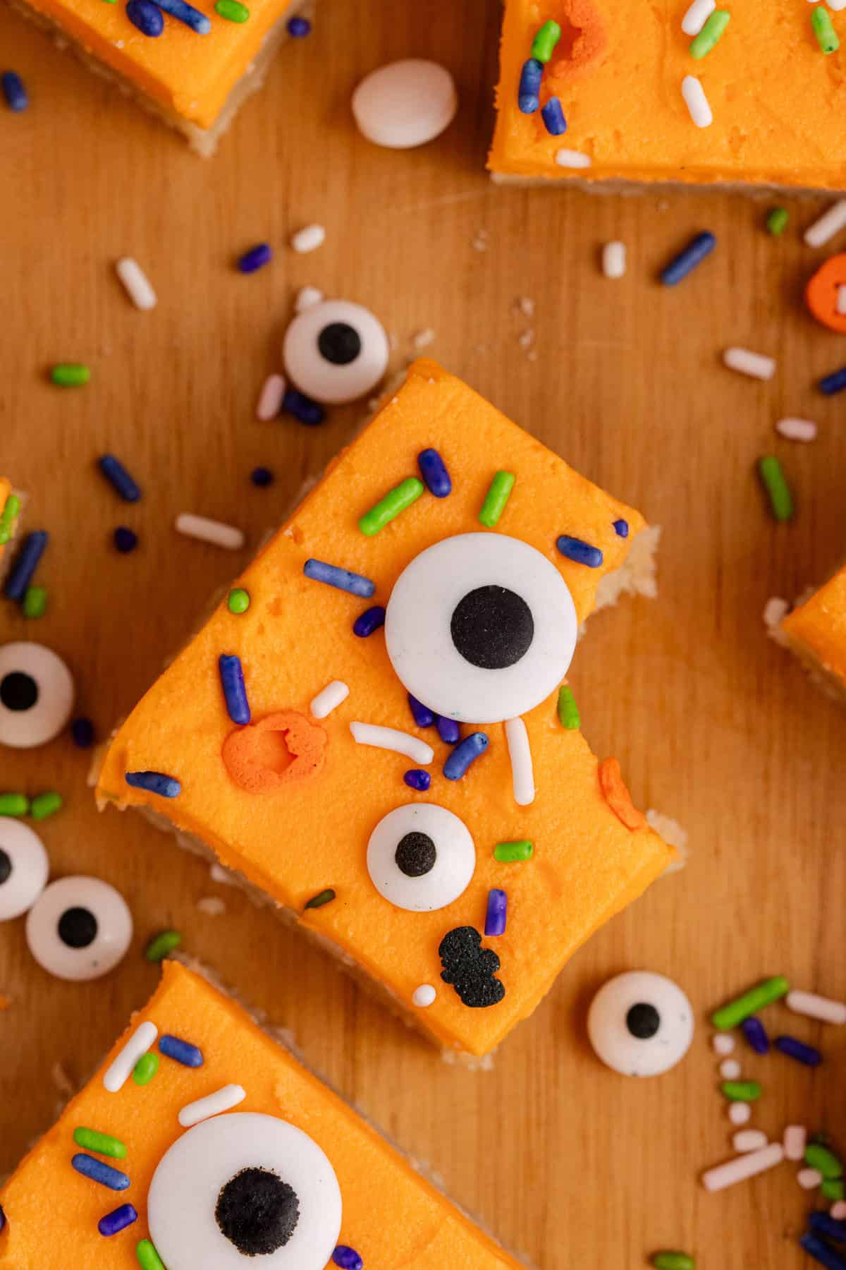 Orange frosted sugar cookie bars topped with candy eyes and colorful sprinkles for Halloween.