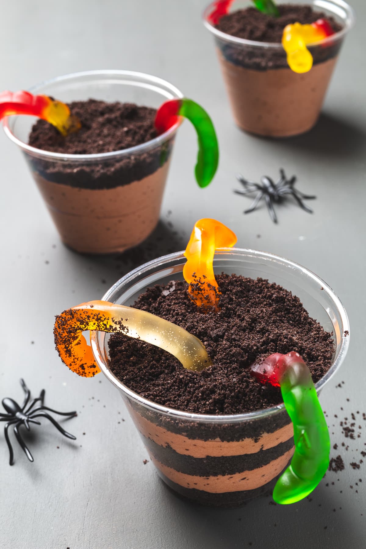 Oreo dirt cup dessert with layered pudding, gummy worms peeking out, and Halloween spider décor.