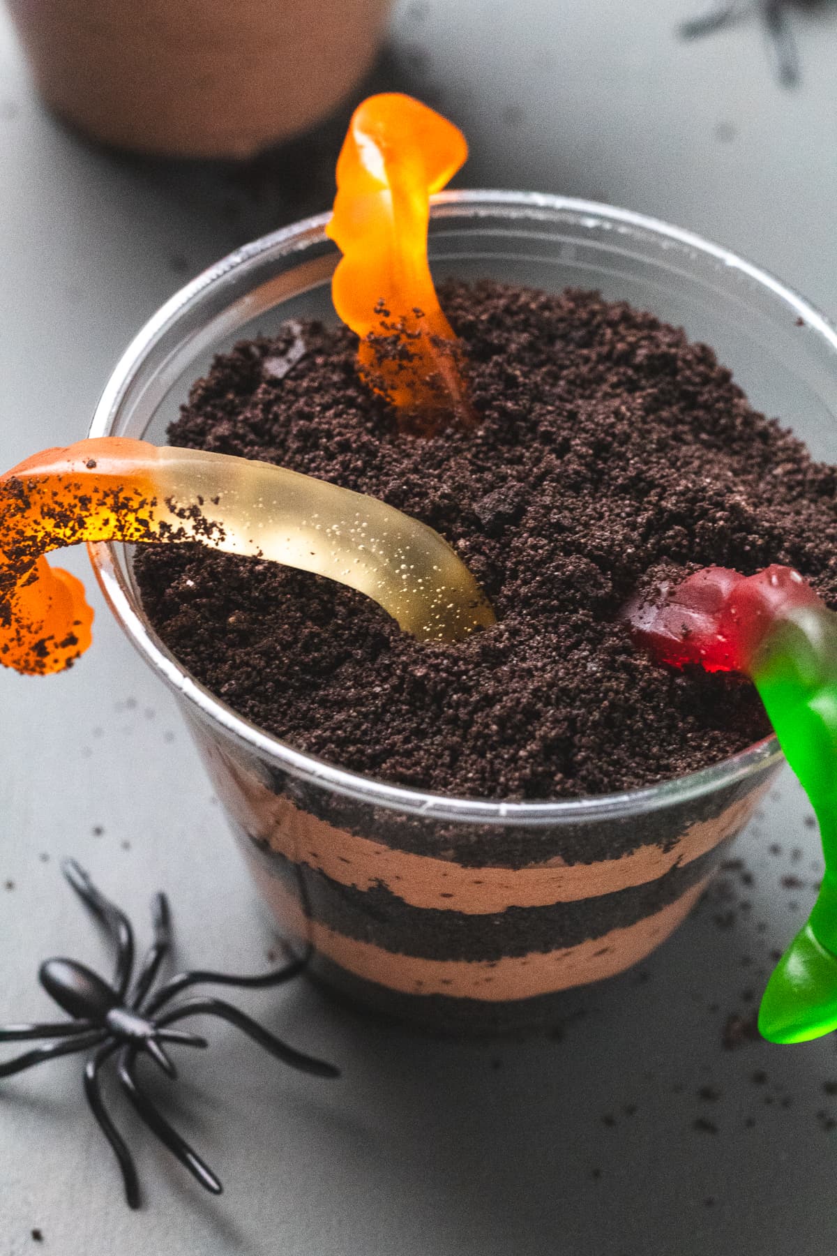 Close-up of Halloween dirt cup layered with Oreo crumbs, gummy worms on top, and a plastic spider.