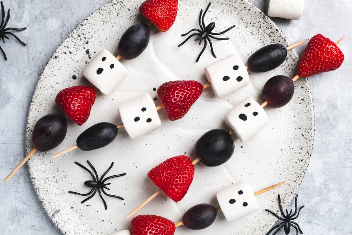 Top-down shot of Halloween skewers with grapes, strawberries, marshmallow ghosts, and spiders for decor.