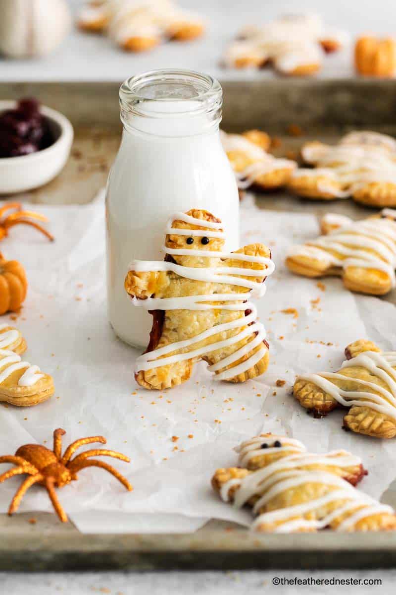 Mummy hand pies drizzled with white icing, styled with milk bottle and toy spiders.