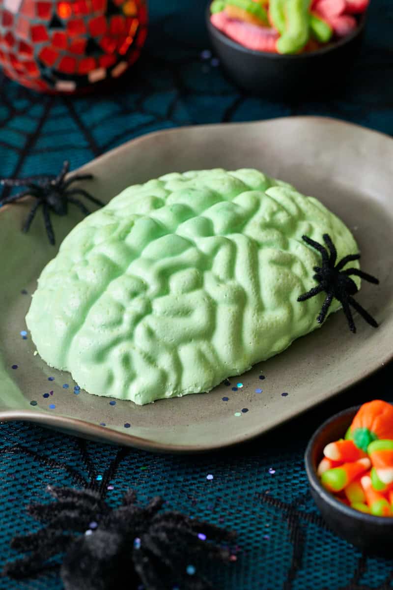 Green jello brain mold on a plate with plastic black spiders and candy, perfect for a Halloween party treat.