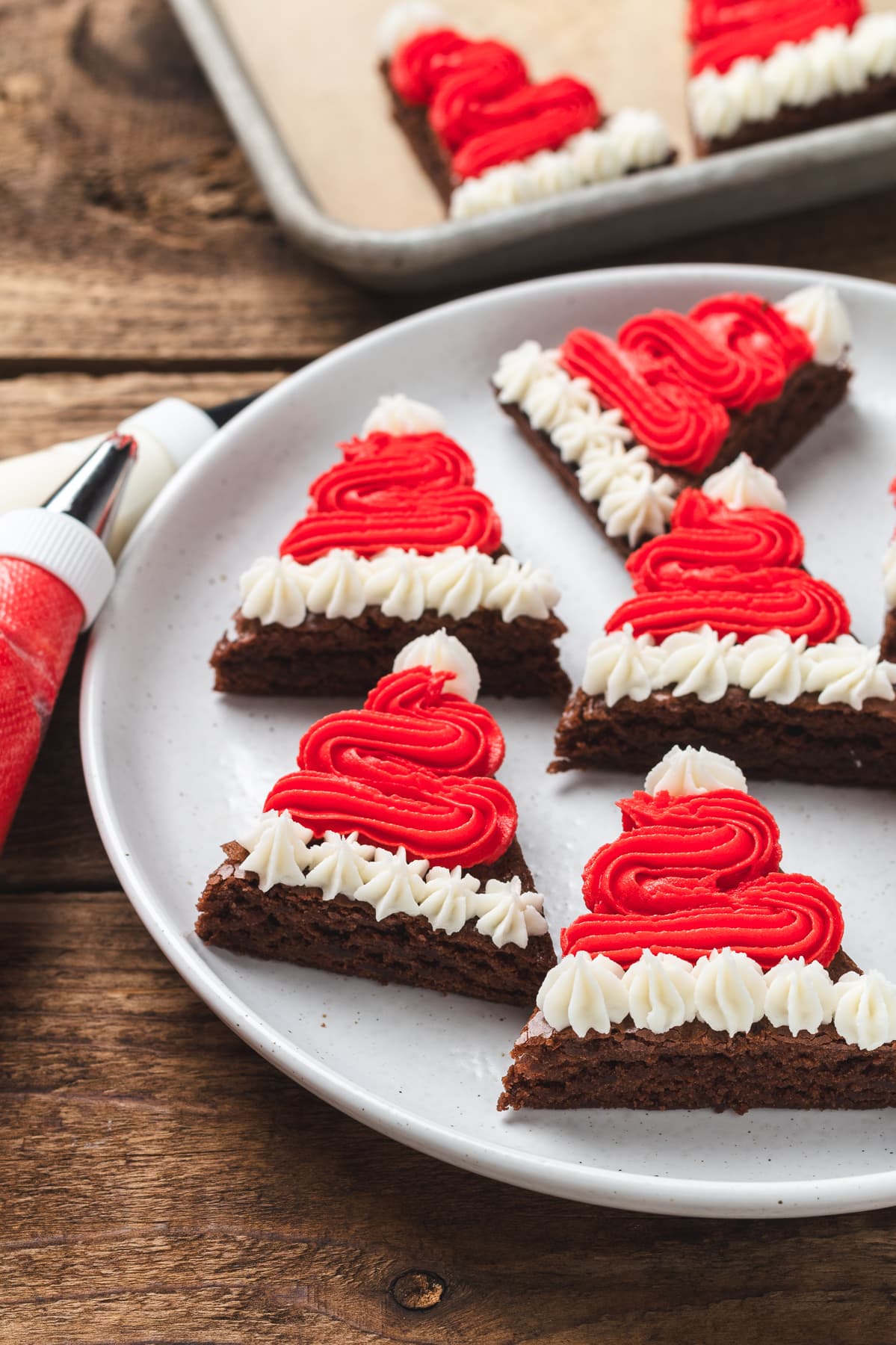 Brownie Santa hat brownies on a plate with piping bags of red and white frosting nearby.