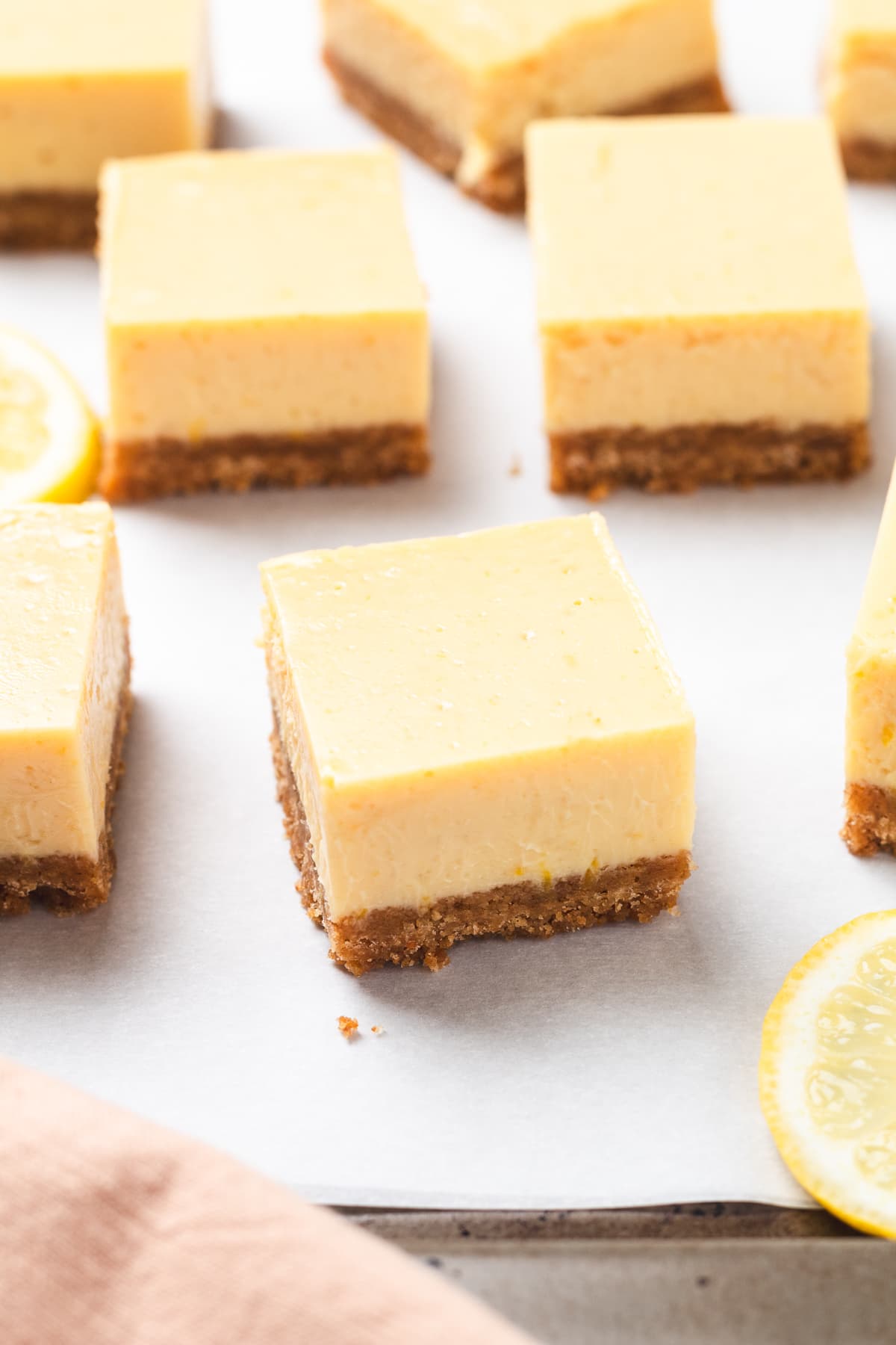 Top-down view of lemon bars on parchment paper with lemon slices.