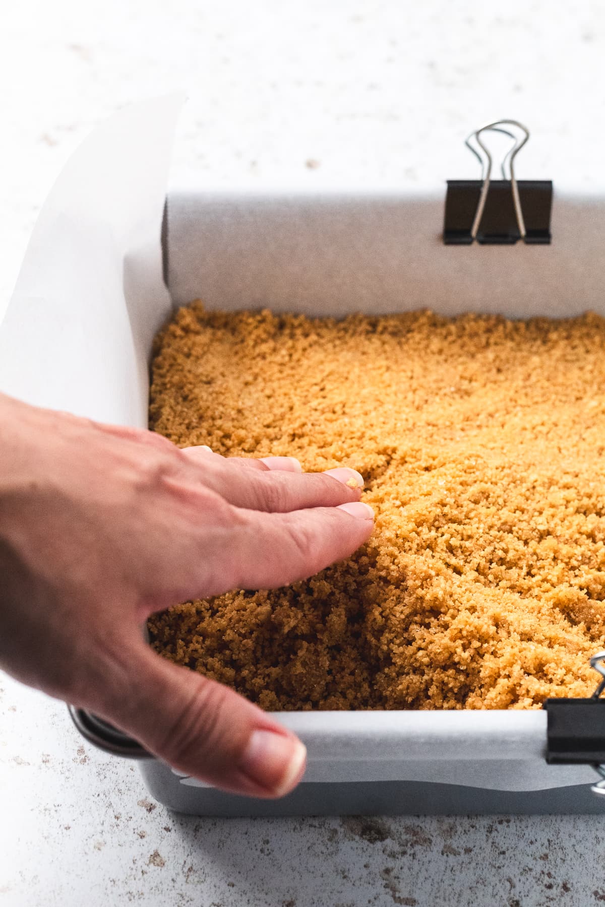 Pressing graham cracker crust mixture into a parchment-lined baking pan.