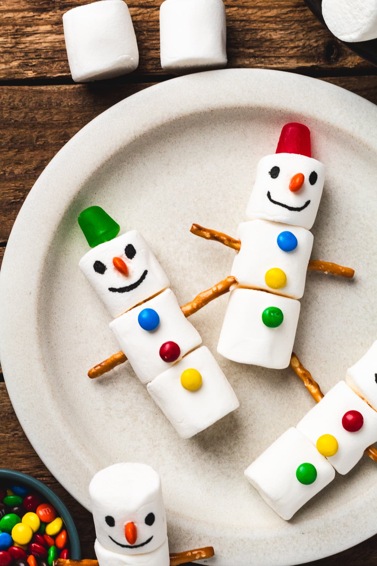 Fun marshmallow snowmen decorated with candy faces, pretzel stick arms, and colorful buttons.