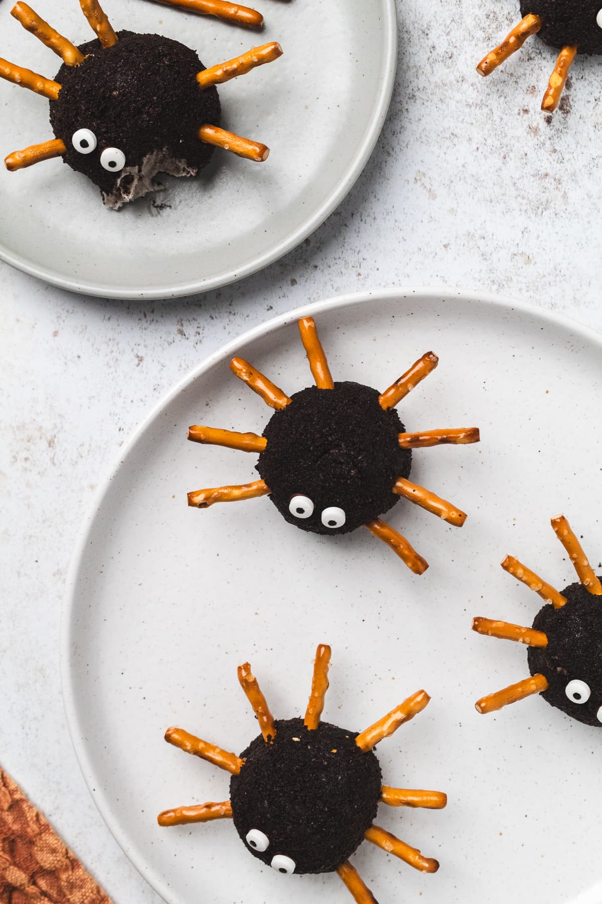 Oreo truffle spiders with pretzel legs and candy eyes arranged on white plates.