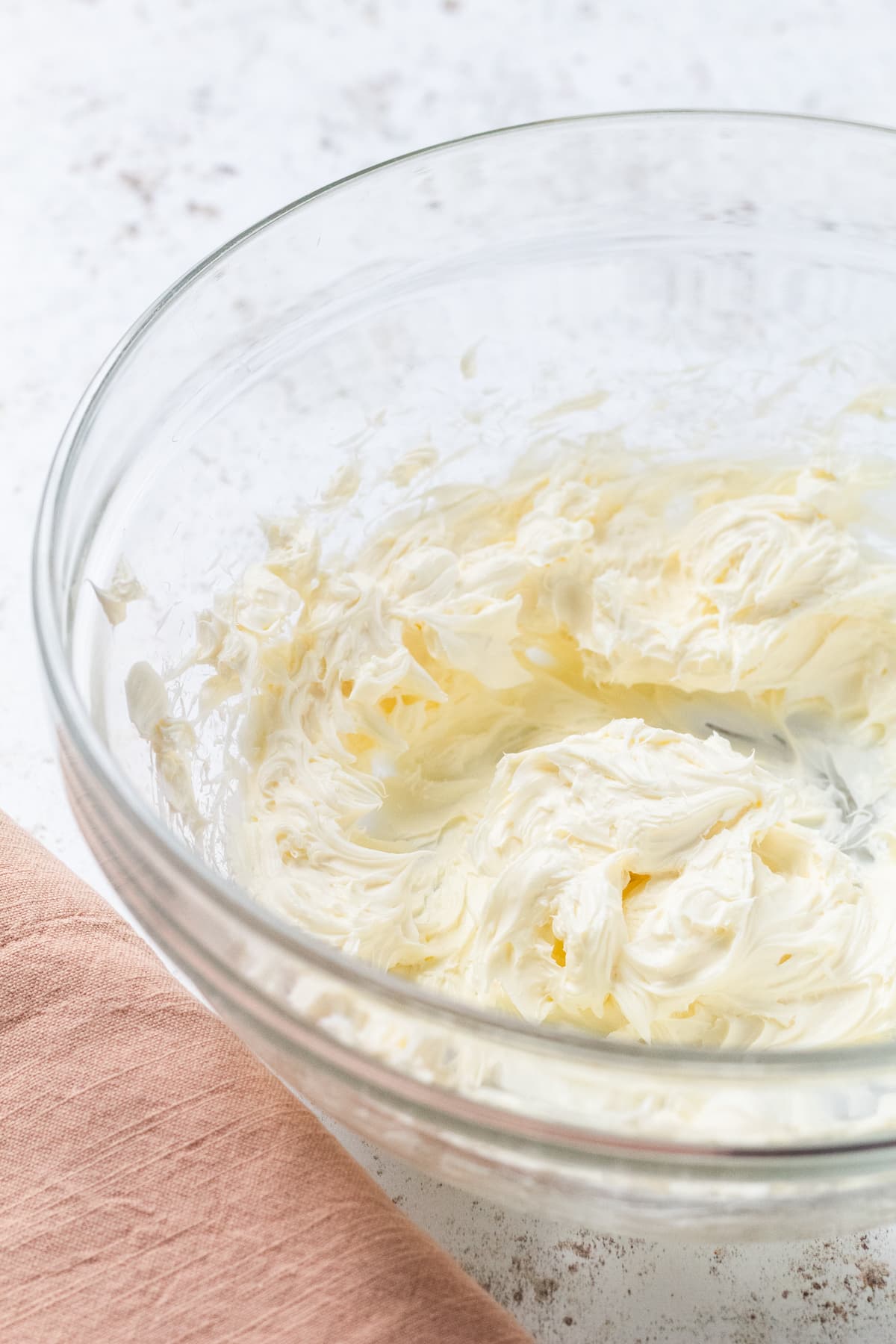 Whipped cream cheese in a clear glass bowl with a peach-colored napkin on the side.