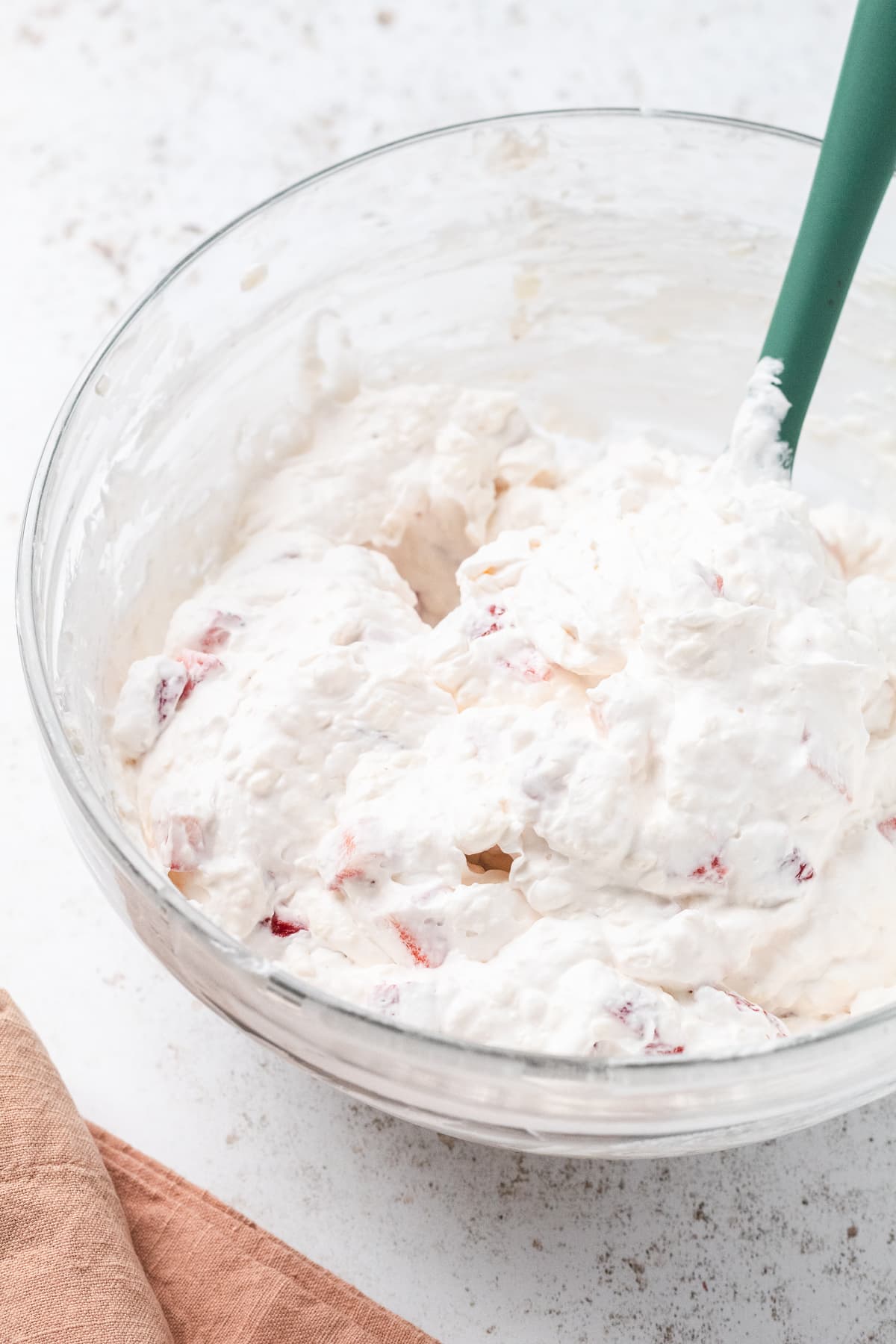 Bowl of strawberry cheesecake dip being mixed with whipped cream and strawberry chunks.