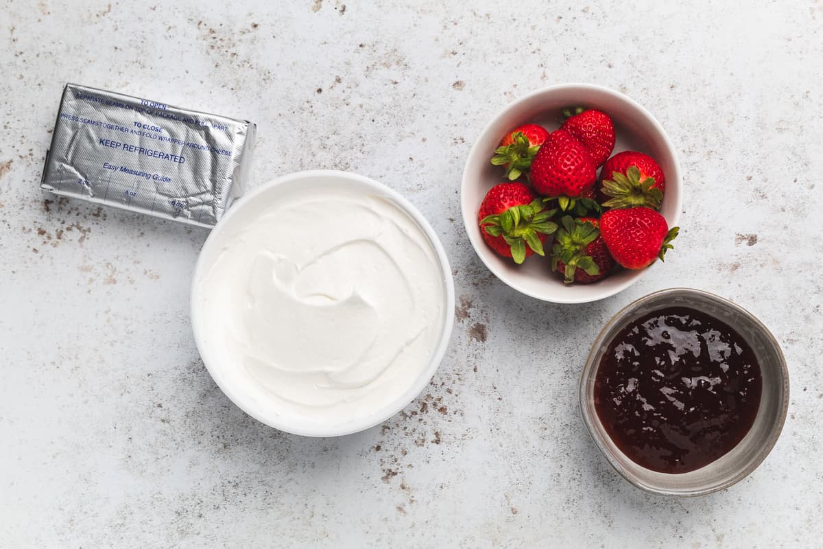 Ingredients for strawberry cheesecake dip including cream cheese, Cool Whip, strawberries, and jam.