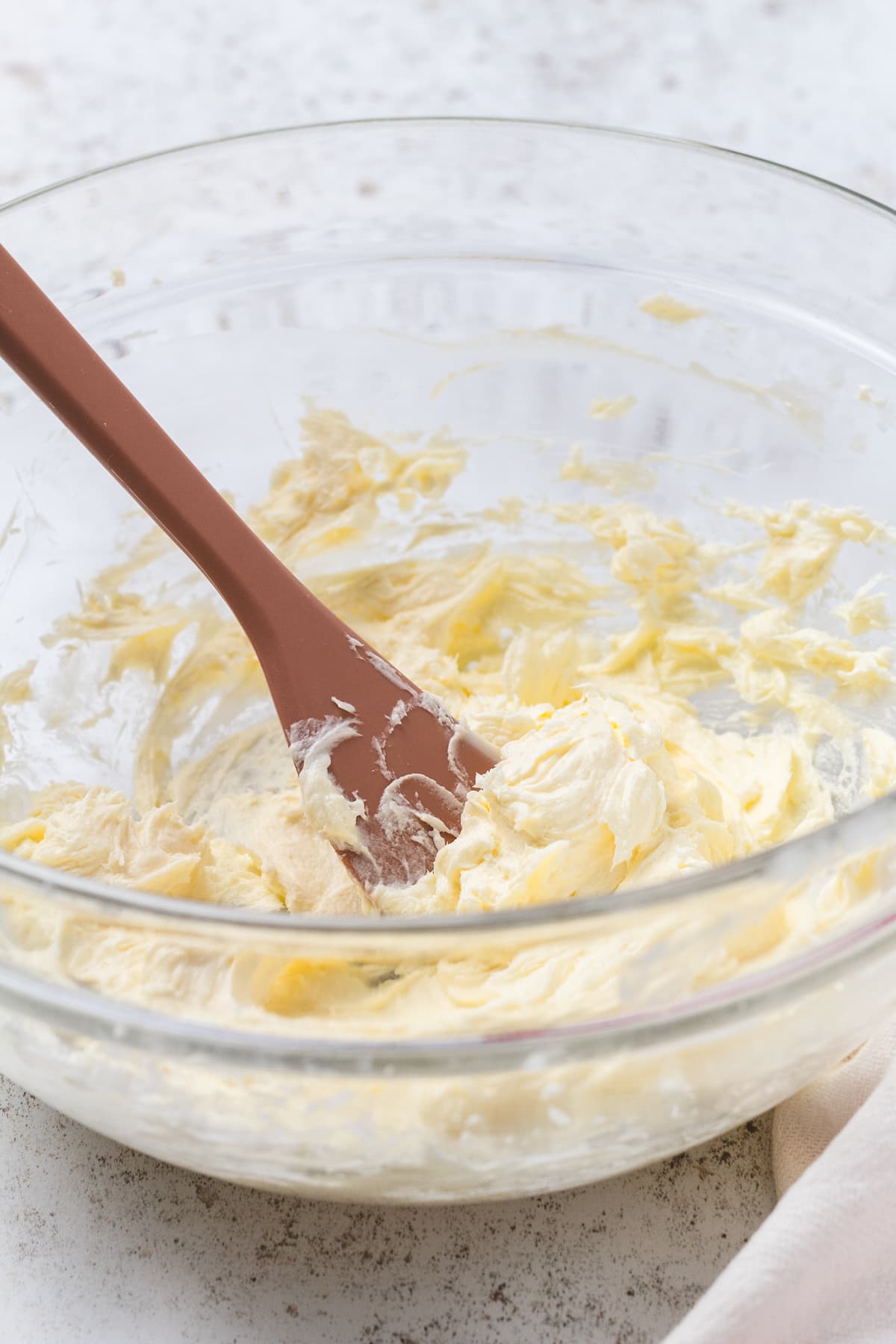 Creamed butter mixture in a glass bowl with a spatula, the base for strawberry cheesecake frosting.