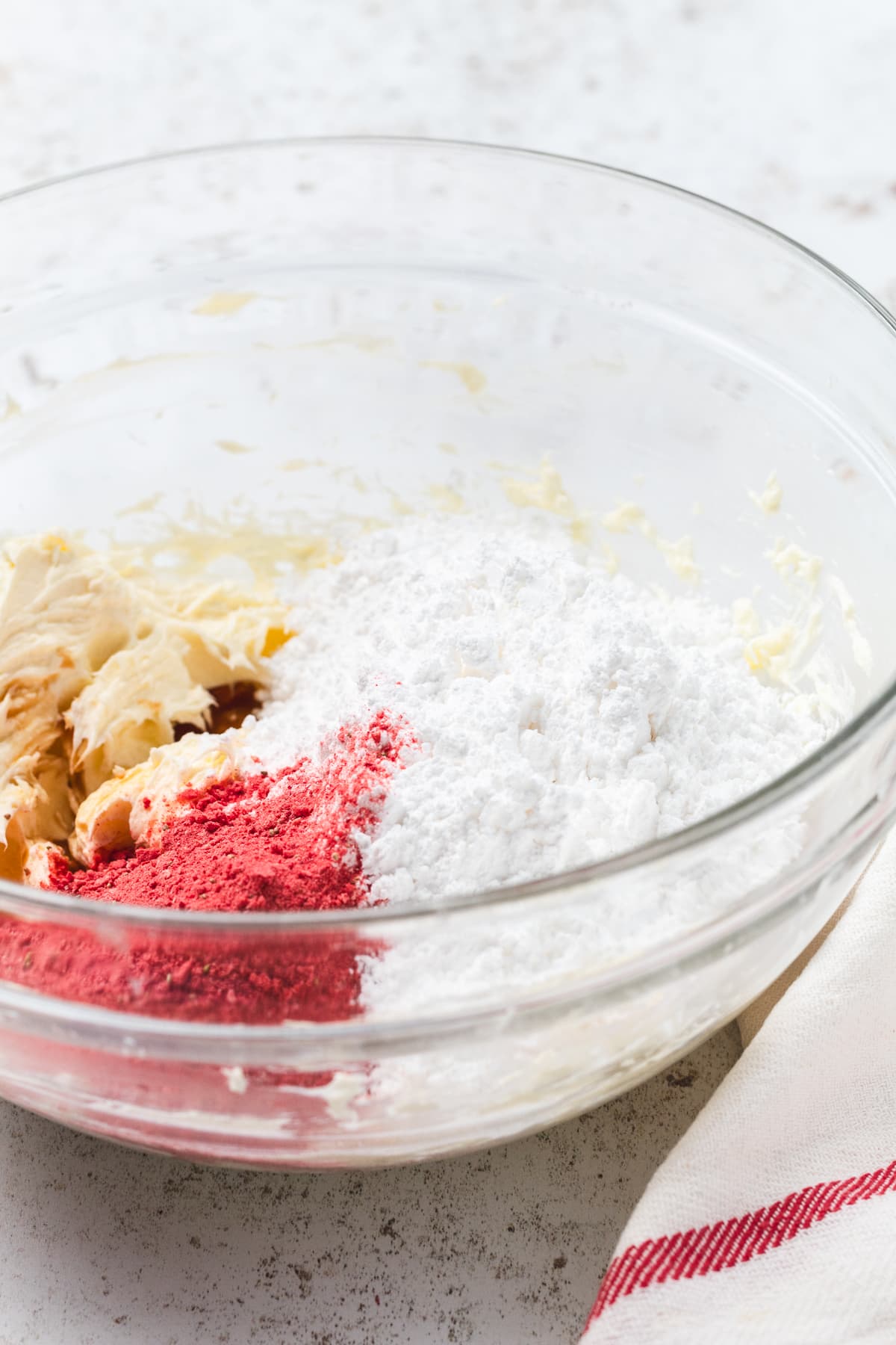 Powdered sugar, butter, and freeze-dried strawberry powder in a glass mixing bowl ready for frosting.